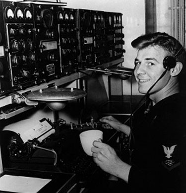 Early communications operator sitting in front of a machine at the Puget Sound Naval Museum.