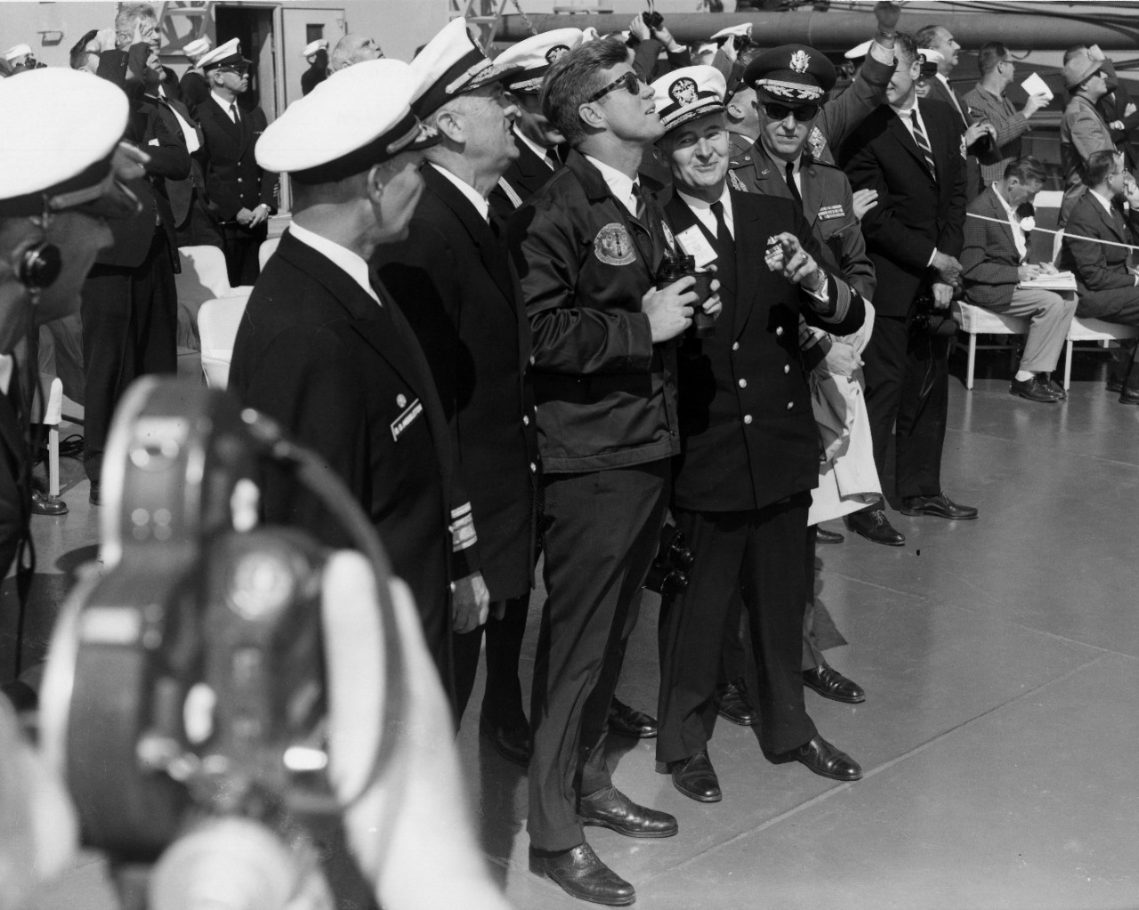 President Kennedy stands with Navy officers and looks to the sky