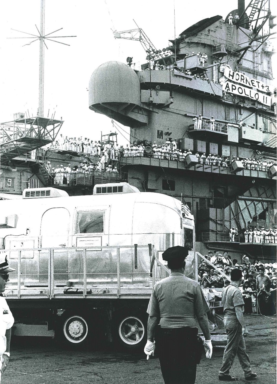 <p>The Mobile Quarantine Facility containing the Apollo 11 astronauts is&nbsp;offloaded from USS Hornet (CVS-12)&nbsp;at Pearl Harbor. One of the astronauts&nbsp;waves from&nbsp;the window.&nbsp;</p>
