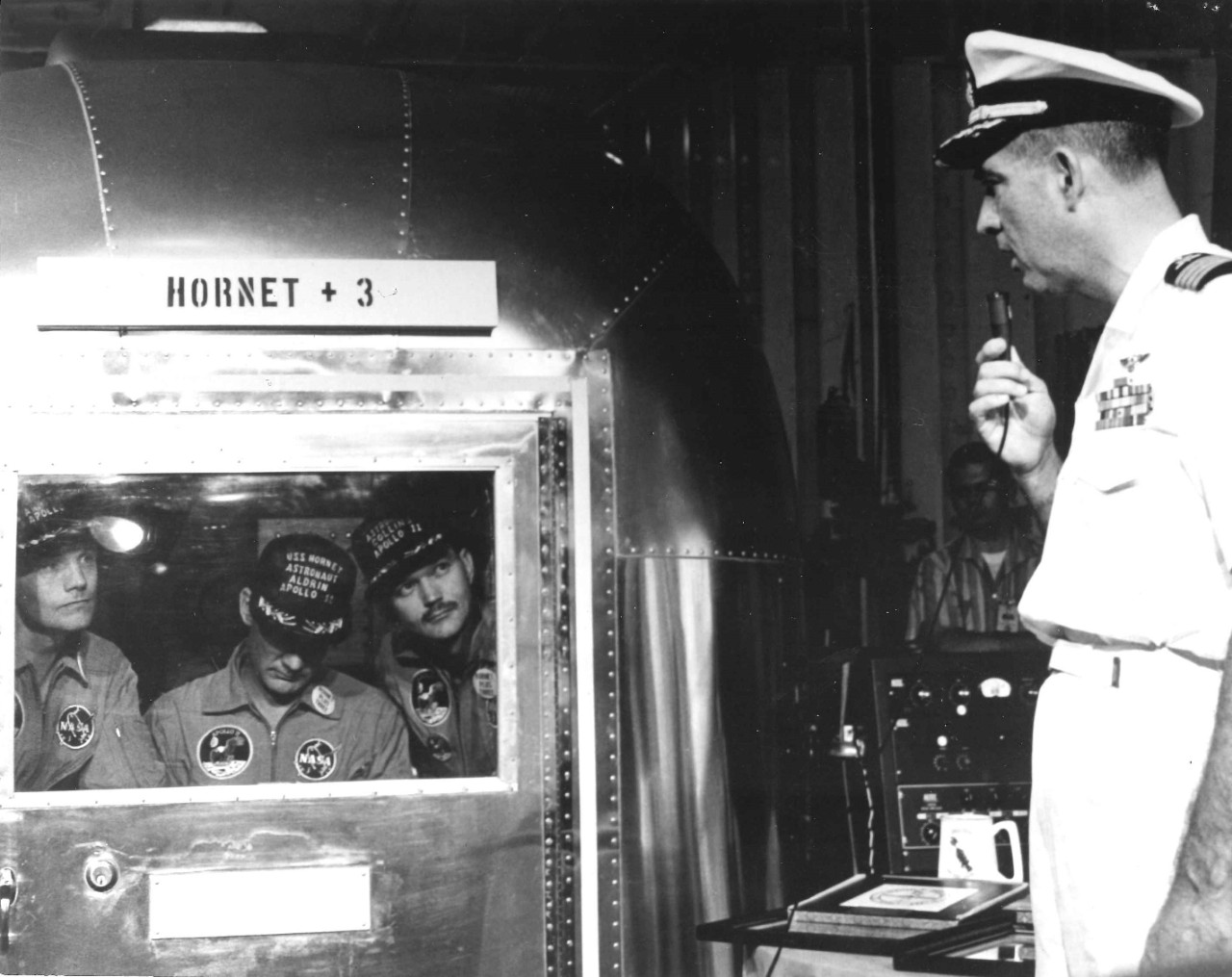 <p>Captain Carl Seiberlich speaks with the Apollo 11 astronauts, who are inside the Mobile Quaratine Facility.</p>
