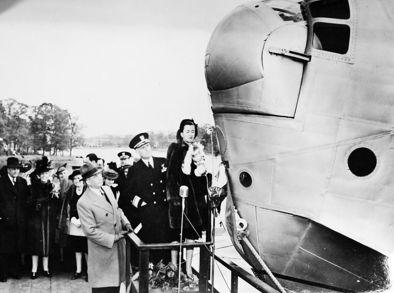 LC-Lot-9827-6: Martin JRM “Mars” aircraft, XPB2M-1, 1941. The giant aircraft was the first flying boat launched with full Naval ceremony, November 8, 1941. Shown: Mrs. Artemus L. Gates, whose husband at that time was Assistant Secretary of the Navy for Air, is about to smash the traditional bottle on the nose of the ship. Looking on are Admiral John H. Towers and Glenn L. Martin. Album from The Glenn L. Martin Company, Baltimore, Maryland, 1941. Courtesy of the Library of Congress. 