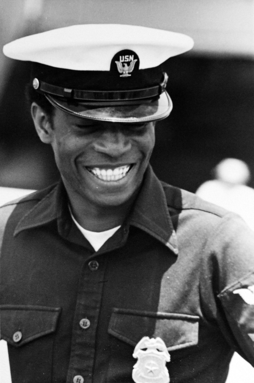 428-GX-USN-1165739:   San Diego, California.   A smiling Master-At-Arms on dock as USS Ranger (CV-61) enters her new homeport.  Photographed by JO2 Scott Day, July 3, 1975.  Official U.S. Navy Photograph, now in the collections of the National Archives.   