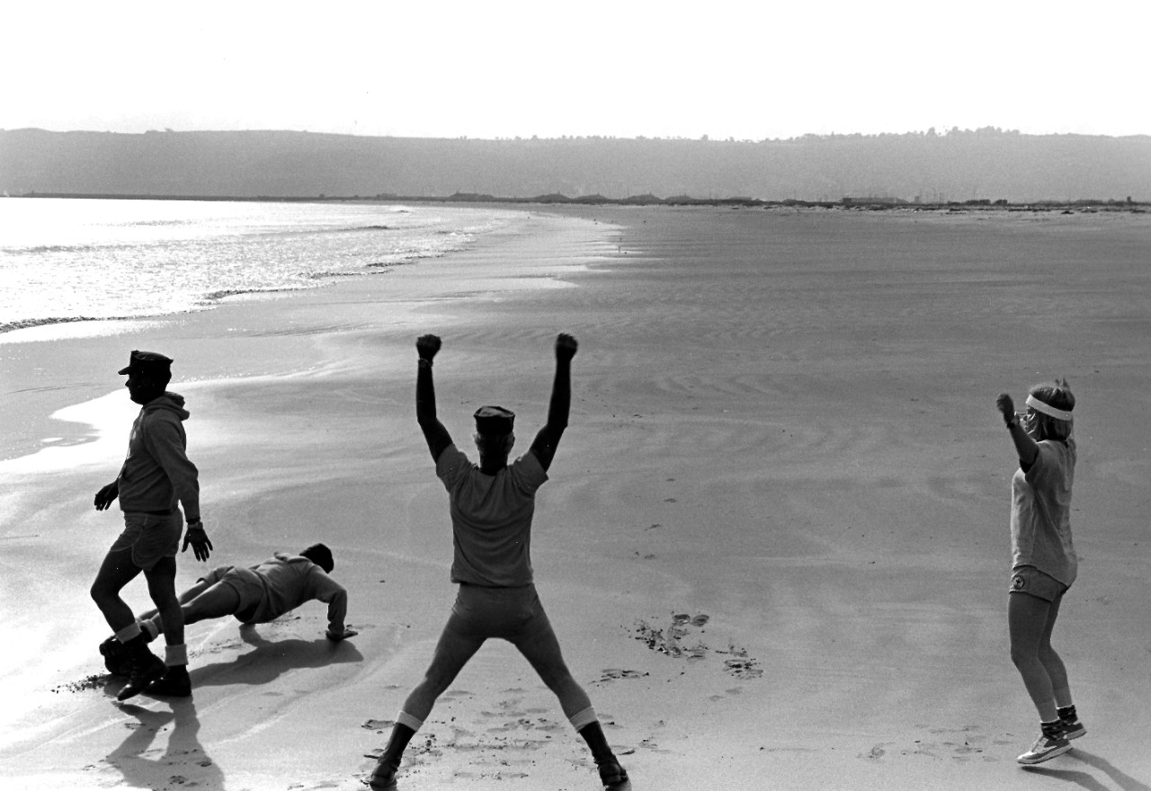 USN 1159679:    Navy Divers, March 1974.   Navy Divers, including Personnelman Seaman (DV) Nancy Garner, the first female Navy diver, do pushups and jumping jacks after running on the beach as part of their daily exercise.   U.S. Naval Air Station, North Island, California, March 25, 1974.  Photographed by AN Harold Brown.   Official U.S. Navy photograph, now in the collections of the National Archives. 