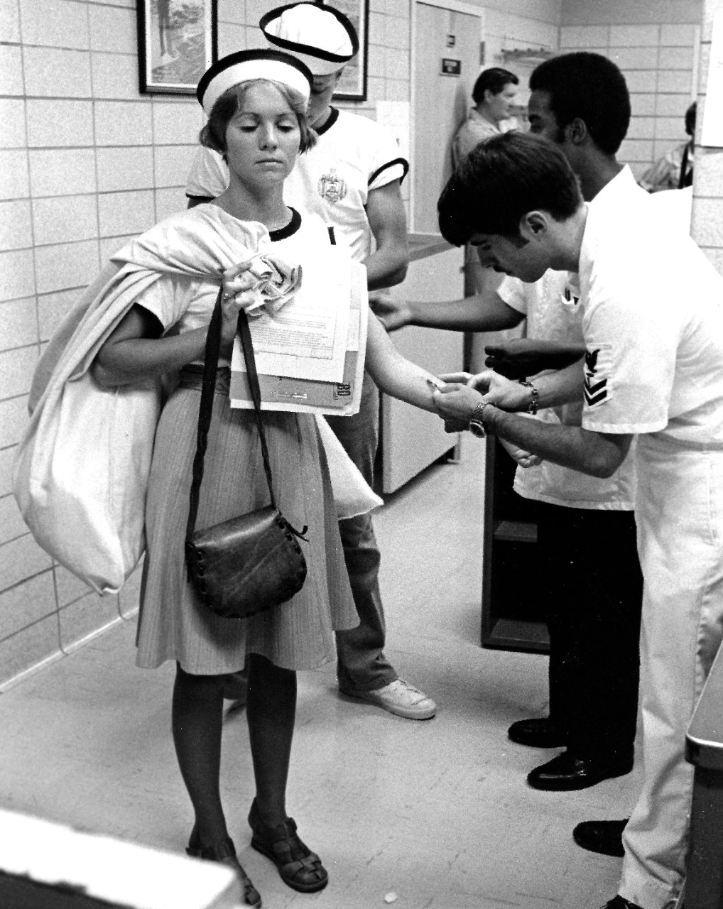 USN 1167421:   Woman Midshipman Janet F. Kotowsky, July 1976.  Kotowsky, receives an inoculation during her stop at the medical station on the day of her arrival at the U.S. Naval Academy, Annapolis, Maryland.  Photographed by PH2 Erich J. Wirth, July 6, 1976.   Official U.S. Navy Photograph, now in the collections of the National Archives.   