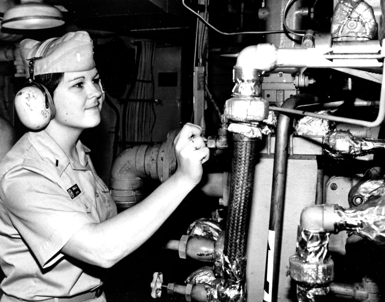 330-CFD-DN-SN-84-01092:   Ensign Roberta McIntyre, November 1981.    McIntyre, the first female to qualify as a Surface Weapons Officer, checks valves aboard the submarine tender USS Dixon (AS-37), where she serves as electrical officer.   Photographed by Delmart Hart, November 1, 1981.   Official U.S. Navy photograph, now in the collections of the National Archives.  