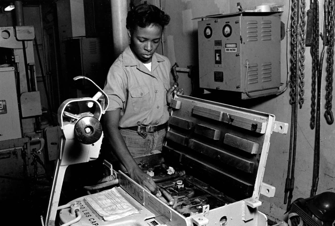 330-CFD-DN-SN-89-03486:  Female crewman onboard USS Cape Cod (AD-43), 1986.   Crewman checks the batteries in an electric pallet jack.   Photographed by PHCS Ron Bayles.   Official U.S. Navy photograph, now in the collections of the National Archives.  