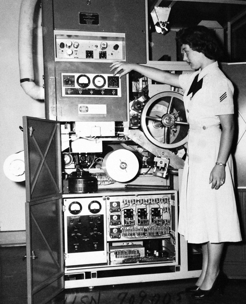 USN 709005:  U.S. Navy High-Speed Facsimile Equipment Developed for Message Transmission, September 1953.   Seaman Geraldine D. Smith points out the Toner Adjustment dial on the Navy’s High-Speed Facsimile equipment, Model CXRG, which is a development model which may be used to transmit virtually any kind of document almost instantaneously over long distances.  The basic system was conceived by engineers of the U.S. Navy’s Bureau of Ships.  Development and construction was carried out under contract with the Radio Corporation of America and the Haloid Company.   The Bureau of Ships found that equipment was needed which would accept copy without processing and would turn out finished copy without need of a “wet” developer or extensive processing.  The Bureau also wanted a machine which would deliver copies that could be directly reproduced on standard office offset-type reproduction equipment.  Previously developed equipment operating at the desired speed required the photographing of copy to be transmitted.  It delivered copy on photographic film, requiring enlarging and printing before delivery to user.  This necessitated expensive equipment, skilled personnel, darkroom facilities and adequate storage space and consumed valuable time, all of which the Navy should to avoid.  It is feasible to install this equipment on larger naval vessels.  The new development makes available a new source of high-speed, high-capacity and low cost service.  Areas of application will not be restricted to the military.  Commercial potential need for such a facility is expected in time to surpass that of the military.  Photograph released September 29, 1953.  Official U.S. Navy photograph, now in the collections at the National Archives.   