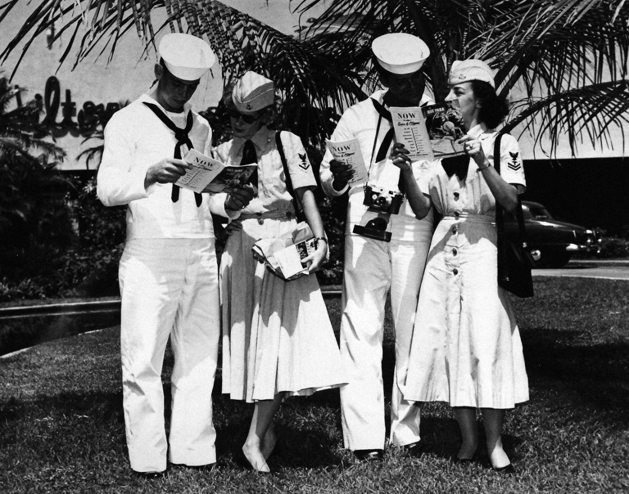 USN 709021:    WAVES and friends on liberty, October 1953.   Posed on the spacious gardens of the Caribe Hilton Hotel while reading the booklet “Que Pasa” (What’s Happening in Puerto Rico), the two couples pause to decide on other points of interest they would be able to see during the afternoon.  Left to right:  Baker, Myers, LaFreniere, and Paluzzi.   Master Caption:   Navy Accepts Women Volunteers for Duty on the High Seas.   For the first time in history, the U.S. Navy has accepted volunteers for duty on the high seas from women in the enlisted WAVES.  Those eligible were WAVES of the Hospital Corps to fill sixty-three billets on ships of the Military Sea Transportation Service.  Photograph released October 26, 1953.   Official U.S. Navy photograph, now in the collections of the National Archives.   