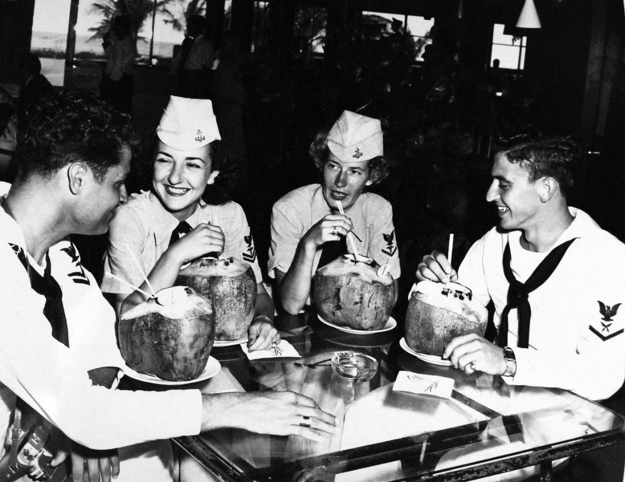 USN 709022:    WAVES and friends on liberty, October 1953.   Yum!  Yum!   The house specialty (chilled coconut milk, served in its original container isn’t sampled, it is consumed veraciously!   The two couples were appreciative guests of the manager of the Caribe Hilton Hotel for refreshments.  Left to Right:  LaFreniere; Paluzzi, Myers, and Baker.    Master Caption:   Navy Accepts Women Volunteers for Duty on the High Seas.   For the first time in history, the U.S. Navy has accepted volunteers for duty on the high seas from women in the enlisted WAVES.  Those eligible were WAVES of the Hospital Corps to fill sixty-three billets on ships of the Military Sea Transportation Service.  Photograph released October 26, 1953.   Official U.S. Navy photograph, now in the collections of the National Archives.   