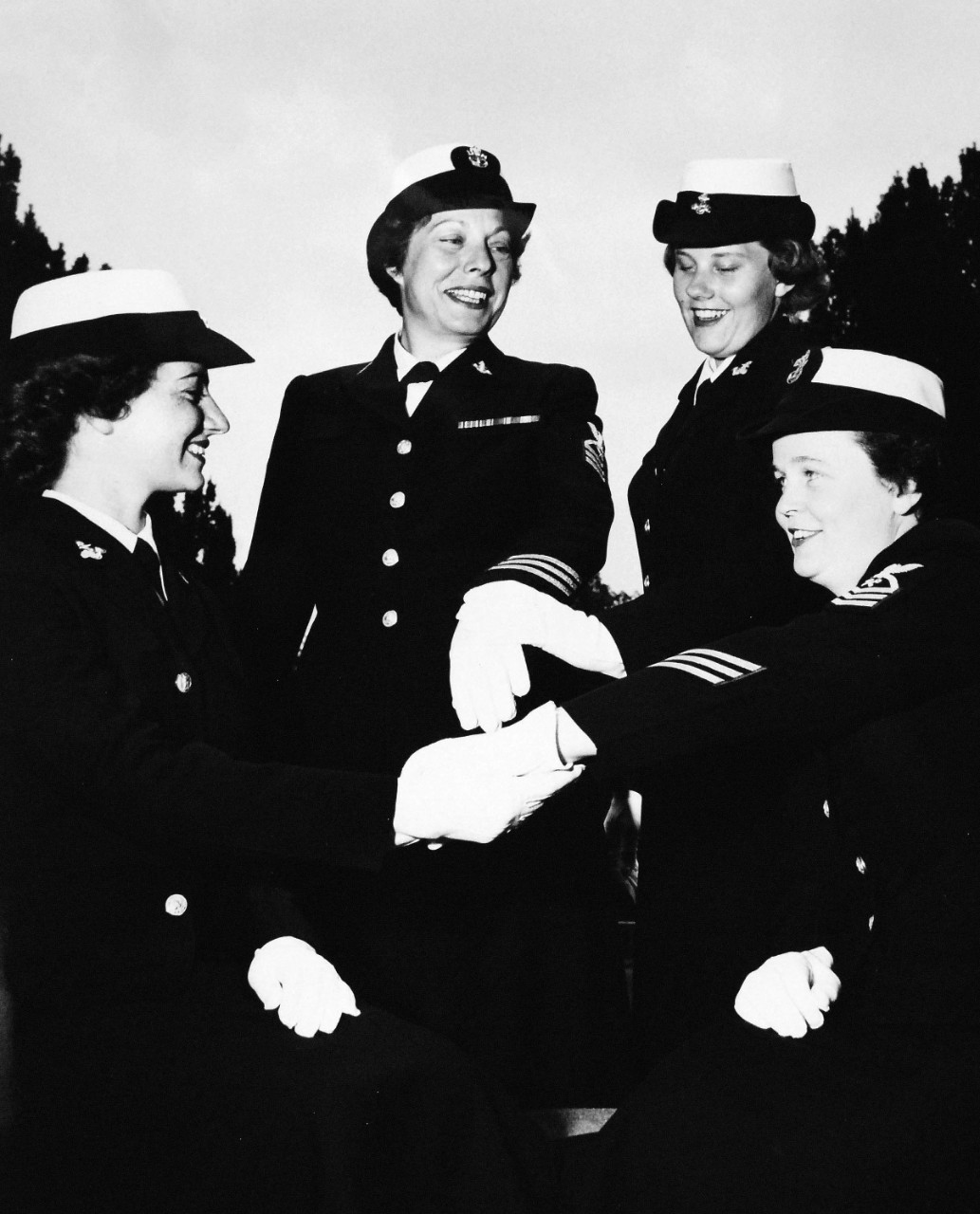USN 709490:   WAVE Veterans on 13th Anniversary of the WAVES, July 1955.  Two veterans who have served with the WAVES since inception, in 1942, display their gold stripes.   Two WAVE “Boots” look on.    Shown, left to right:   Seaman Apprentice Laura Quaid; Chief Yeoman Leo; Seaman Apprentice Virginia Scott; and Chief Storekeeper Margaret Gay.   Master Caption:  WAVES Observe 13th Anniversary:   Preparatory to their Thirteenth Anniversary, July 30, WAVE Recruits at the Naval Training Center, Bainbridge, Maryland, pass in review.  These young women will take their places with sailors in important technical and clerical duty assignments both at home and abroad.  At that time, there were approximately 7,000 WAVES on active duty in the U.S. Navy.   Photograph released July 25, 1955.  Official U.S. Navy photograph, now in the collections of the National Archives.   