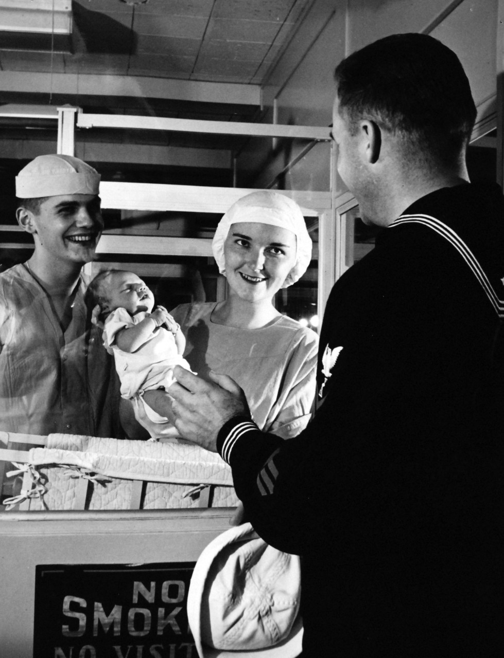 USN 709747:   A U.S. Navy Nurse and others a nursery, January 1957.   A proud sailor smiles approvingly as he sees his infant son for the first time.  In charge of the Nursery at the U.S. Naval Hospital, Bethesda, Maryland, is Navy Nurse, Lieutenant Junior Grade Virginia M. McGuigan, NC, USNR.   Assisting her is Hospital Corpsman Third Class Paul J. Altman, Jr.   Caring for dependents of military personnel is only one of the many duties of a Navy Nurse.  Photograph released January 4, 1957.  Official U.S. Navy photograph, now in the collections of the National Archives.   