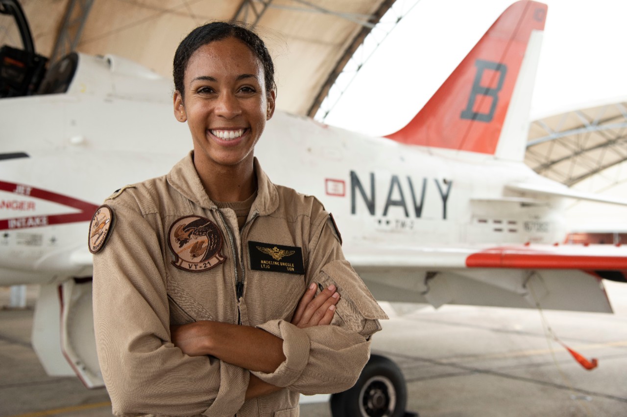 200717-N-OU681-1014:   Lieutenant Junior Grade Madeline G. Swegle, 2020.   Swegle, the U.S. Navy’s first African American female tactical jet aviator, stands in front of a T-45C Goshawk jet trainer aircraft on the Training Air Wing 2 flight line at Naval Air Station, Kingsvile, Texas, July 17, 2020.  Swegle completed her final training flight with the “Redhawks” of Training Squadron 21 and was soft winged July 7.   Her official winging ceremony is scheduled July 31 after which she will continue to graduate training at her fleet replacement squadron.  TW-2 is one of five air wings under the Chief of Naval Air Training and conducts intermediate and advanced jet training for the Navy, Marine Corps, and international military partners.  Photograph by Lieutenant Michelle Tucker.   Official U.S. Navy Photograph.  