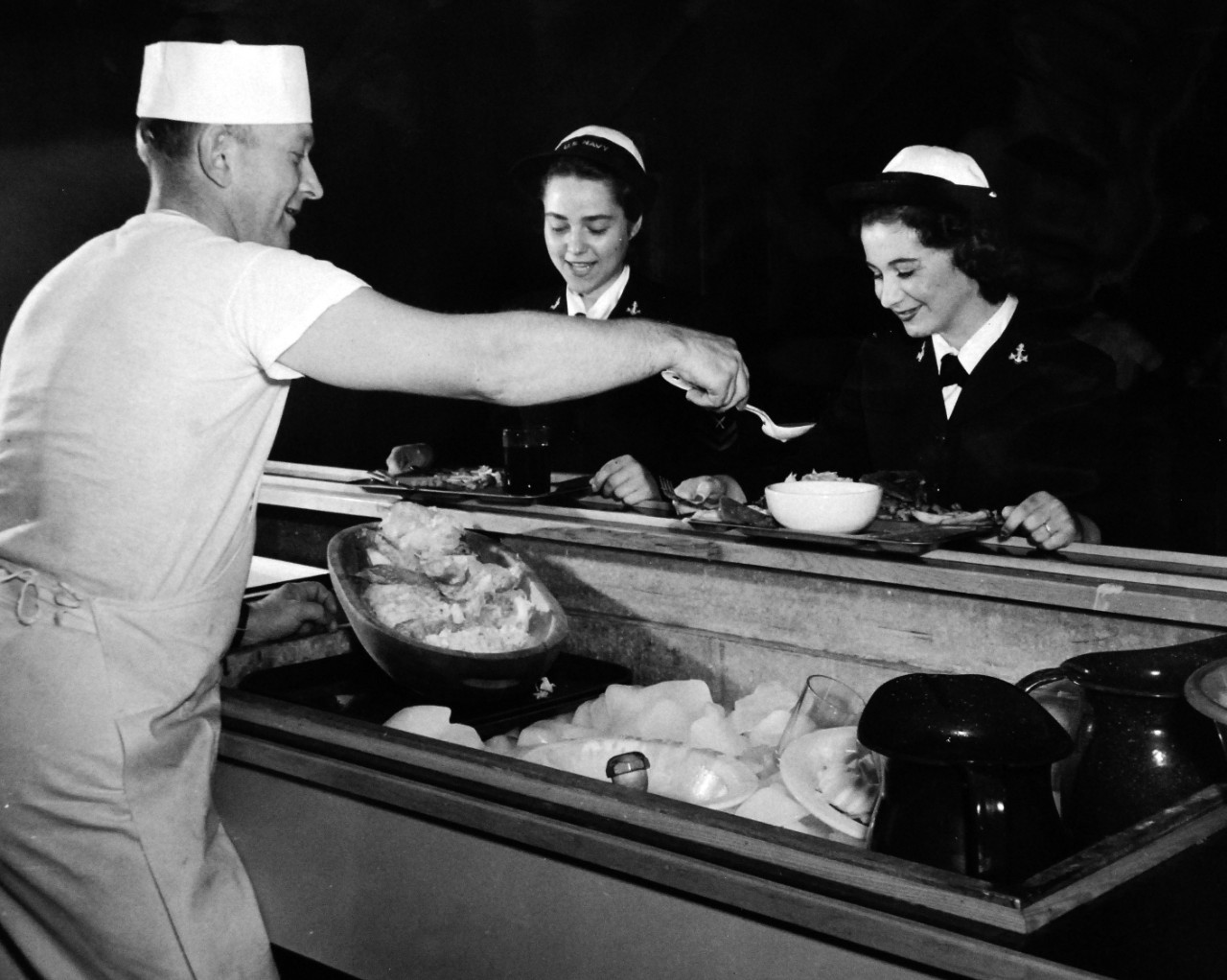 80-CF-8811-14_Box 175:  Naval Air Station, Pasco, Washington, July 1943.  Pleased with their Navy chow are these two WAVES who look on approvingly as Ship’s Cook Second Class H.D. Hawley adds a dash of special dressing to a salad.  Though the Navy does not pamper the Women’s Reserve, nevertheless, it believes in offering them special dishes so appreciated by women.  The women are, (from the left), Yeoman Second Class Alice Evans and Seaman Second Class Donna Huston.   Official U.S. Navy photograph, now in the collections of the National Archives 