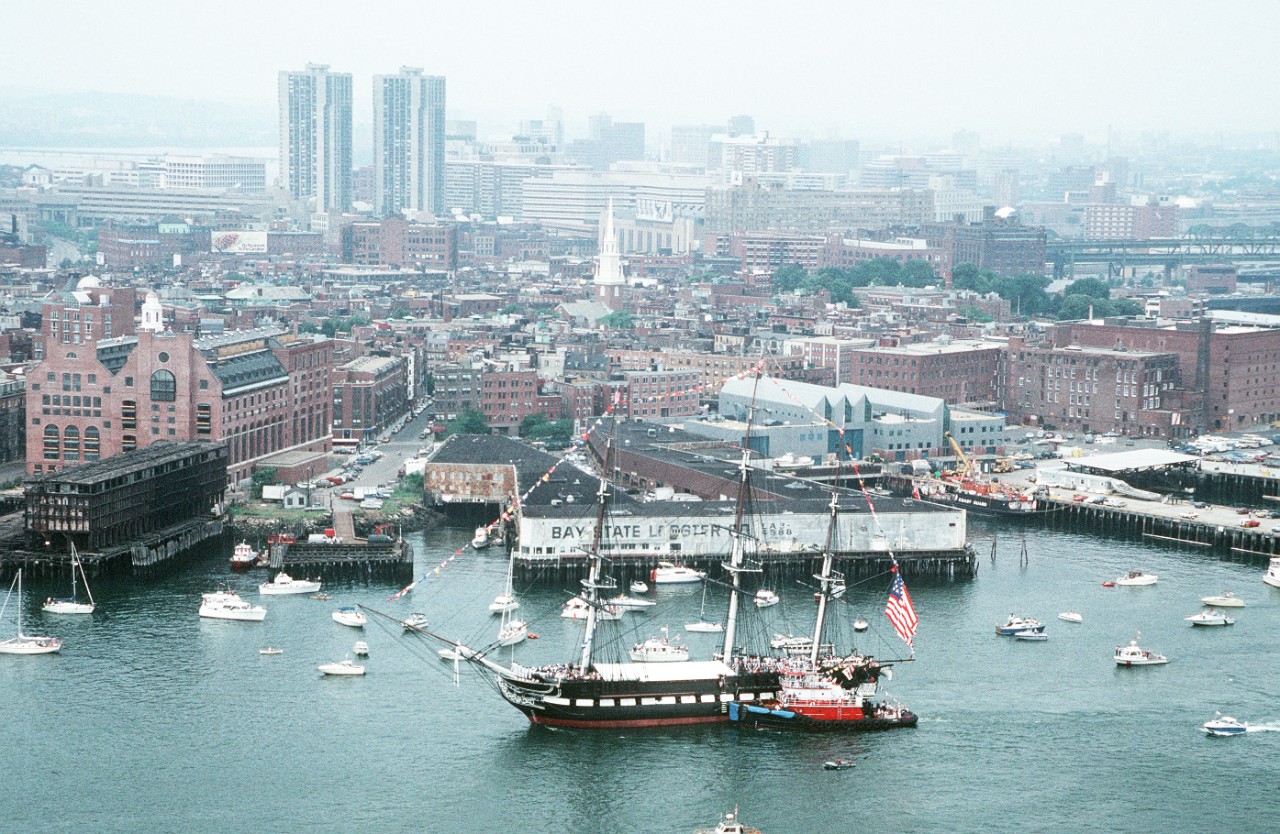 330-CFD-DN-ST-87-11231:   USS Constitution, 1986.   An aerial view of the 44-gun sail frigate USS Constitution being assisted by a fire tug during the ship's annual turnaround cruise in the harbor, July 4, 1986. After a 21-gun salute to the nation, the ship will be returned to its berth facing the opposite way to help it weather evenly and preserve the wood.   Photographed by Lieutenant Emmett Francois.   Official U.S. Photograph, now in the collections of the National Archives.  