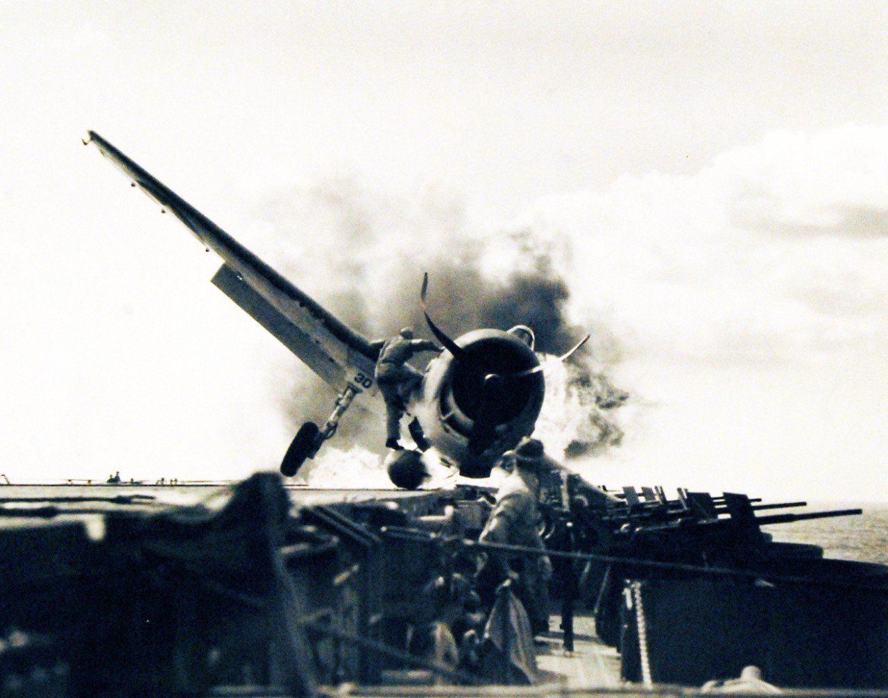 80-G-205473: USS Enterprise (CV-6). 1943.      Crash landing of F6F #30, piloted by Ensign Bryon M. Johnson on the flight deck while enroute to attack Makin Island in the Gilbert Islands.   Lieutenant Walter L. Chewning, USNR, catapult officer, clambering up the side of the plane to assist pilot Ensign Johnson, from the flaming cockpit.  Johnson escaped with little personal damage.   Photograph released November 10, 1943.    Official U.S. Navy photograph, now in the collections of the National Archives.  (2016/11/15).