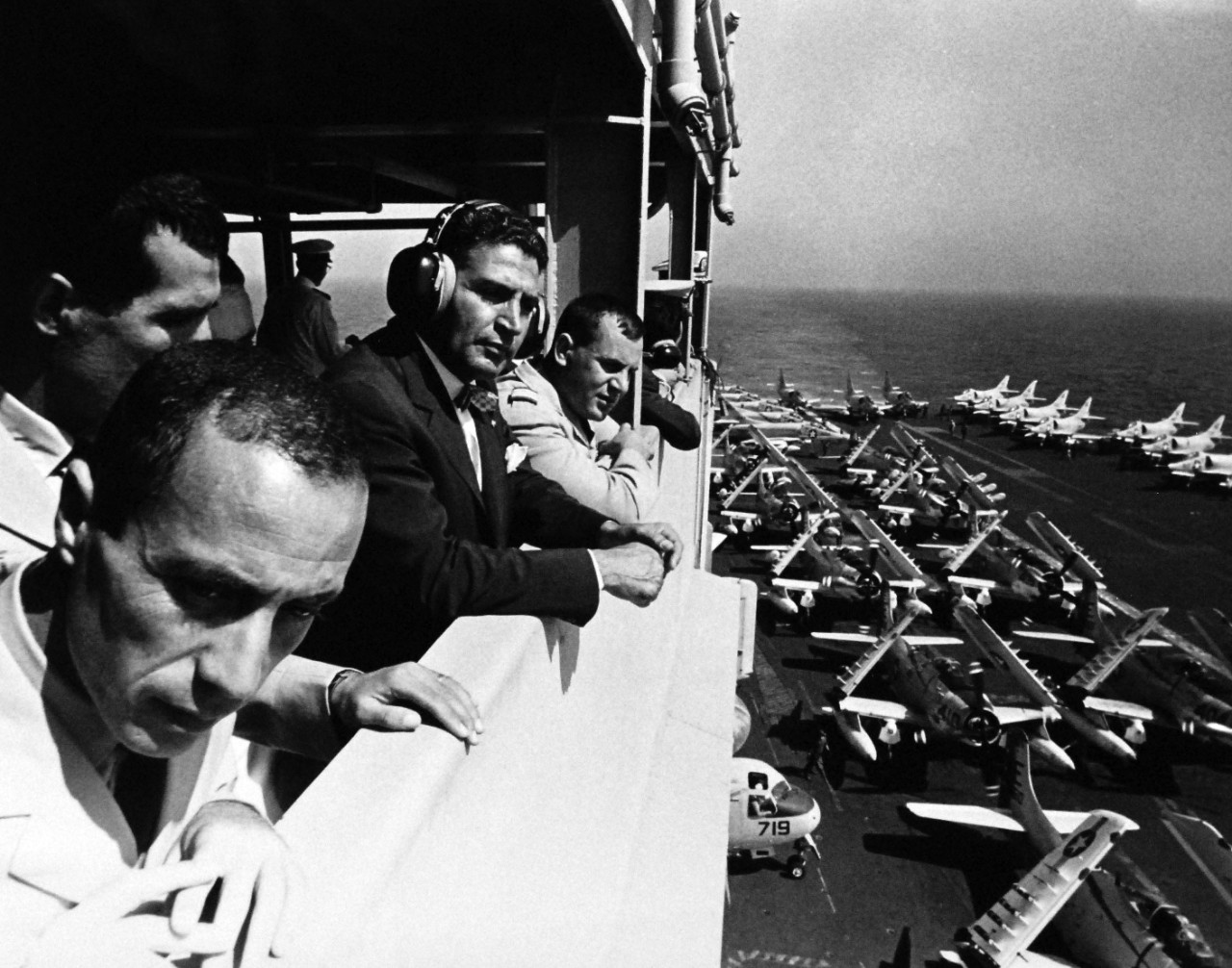 330-PSA-178-64 (USN 1104219E):  Operation Sea Orbit, 1964.   Members of the Moroccan Chamber of Counselors watch flight operations onboard USS Enterprise (CVN 65) during an underway visit off the coast of Africa.  Master caption:  Operation Sea Orbit has completed the first three weeks of its round-the-world cruise proving conclusively the feasibility of operation nuclear surface ships over great distances on a self-sustaining basis.  Sea Orbit is the first world cruise of the surface nuclear ships.  The task force is made-up of USS Enterprise (CVN-65), USS Long Beach (CLGN-9), and USS Bainbridge (DLGN-25).   The world cruise has a dual mission.  It offers practical experience in operation of nuclear-powered warships independent of support ships, a fast impractical for conventionally powers ships.  Equally important, and immediately evident is the opportunity to win friends in areas not frequently visited by U.S. Navy ships, and to show the world an all nuclear element of the world’s greats power for peace.  Two other world circumnavigations were made by U.S. nuclear vessels, both submarines.  Photograph released August 22, 1964.  Official U.S. Navy Photograph, now in the collections of the National Archives.   (2015/11/03).