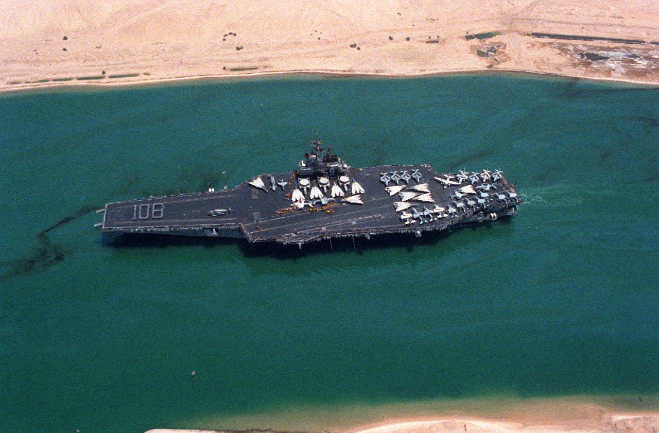 330-CFD-DN-SC-89-02509:  USS Forrestal (CV-59), 1988.  Aerial port beam as the aircraft carrier transits the Suez Canal.  A formation of crewmen spells out 108 on the bow to signify that the ship has been at sea for 108 consecutive days, August 6, 1988.    Photographed by PH2 Buckner.   Official U.S. Navy Photograph, now in the collections of the National Archives.    