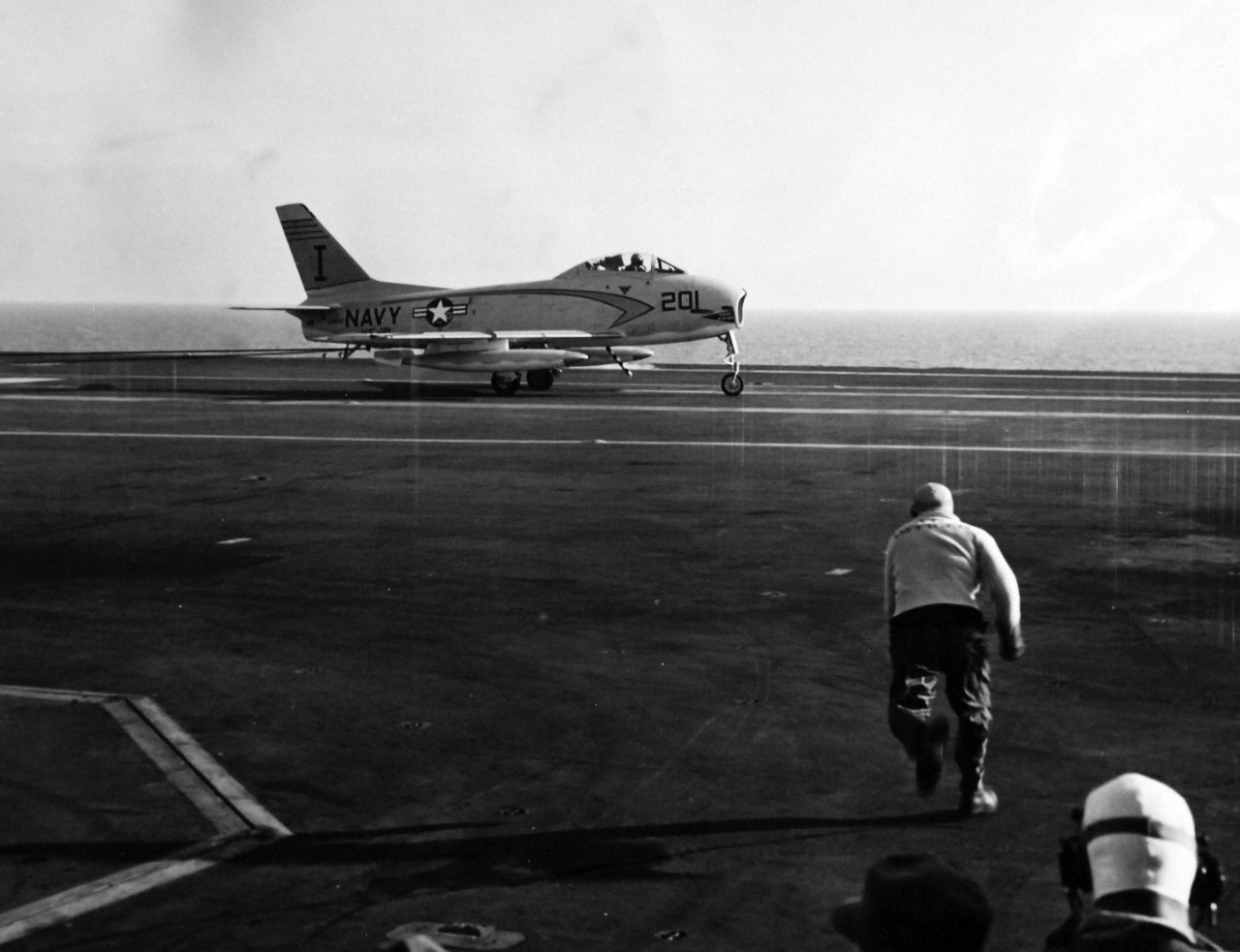 330-PS-7642 (USN 684244):  USS Forrestal (CVA-59), 1956.    Crewmen dash to receive the second jet landing onboard USS Forrestal (CVA-59).  This U.S. Navy FJ-3 “Fury” was piloted by Commander W.M. Harnish, USN.   The first jet landing was performed by Commander R. L. Werner, USN.  Werner commanded Air Task Group 181 (ATG-181) and landed approximately 2:40 (EST), January 3, 1956 while the aircraft carrier, operating at sea east of Norfolk, Virginia, was undergoing a series of routine tests.  Commander Werner made three touch-and-go landings before making the first full-stop landing.  A few hours later, piloting the same aircraft, he also made the first catapult launch from the carrier.   Aircraft used for these trials are based at the U.S. Naval Air Station, Oceana, Virginia.  Later, at approximately, 2:45 (EST), Commander W.M. Harnish, USN, Commanding Officer, Squadron 21 (a unit of ATG-181), piloting a U.S. Navy FJ-3 “Fury” made the second landing on board Forrestal.    Commander Harnish’s father, Mr. W.E. Harnish, was the Professor of Education at the University of Illinois.  Lieutenant Vincent Darcey, USN, of ATG-181, was the Landing Signal Officer for both landings.  Both aircraft were painted with the new white and grey “atomic” paint scheme.    Photograph released January 4, 1956.   Offical U.S. Navy Photograph, now in the collections of the National Archives.  (2015/02/18)  