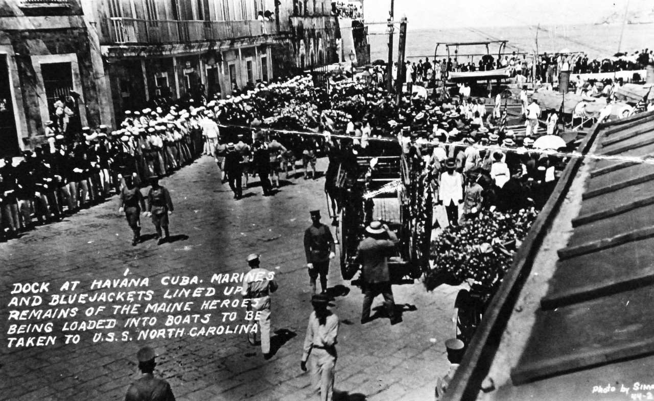 80-G-680173: USS Maine (1895-98), March 1912.  US Sailors and Marines lined up on dock at Havana, Cuba, March 1912.  Remains of the Maine heroes being loaded into boats to be taken to USS North Carolina (Armored Cruiser #12), 14 September 1955.   Official U.S. Navy Photograph, now in the collections of the National Archives. (2014/04/03).    