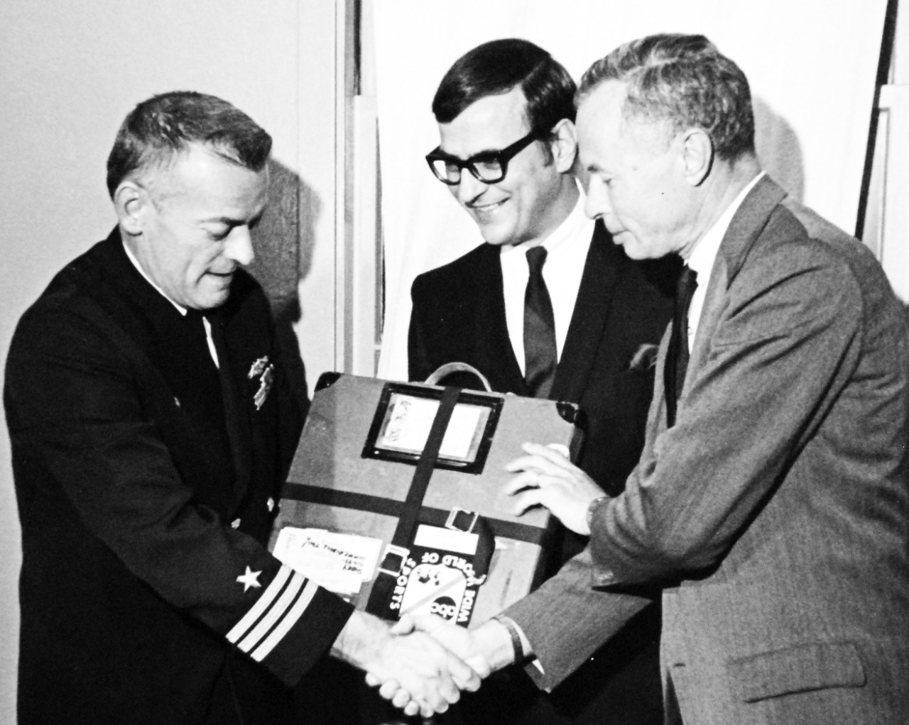 428-GX-USN-1140158:   U.S. Naval Air Station, North Island, California, February 6, 1969.    Commander Lloyd M. Bucher, Commanding Officer of USS Pueblo (AGER-2) receives a gift from the American Broadcasting Company’s “Wide World of Sports” program personnel during a party.  Official U.S. Navy Photograph, now in the collections of the National Archives (2017/05/23).  Photographed from reference card. 