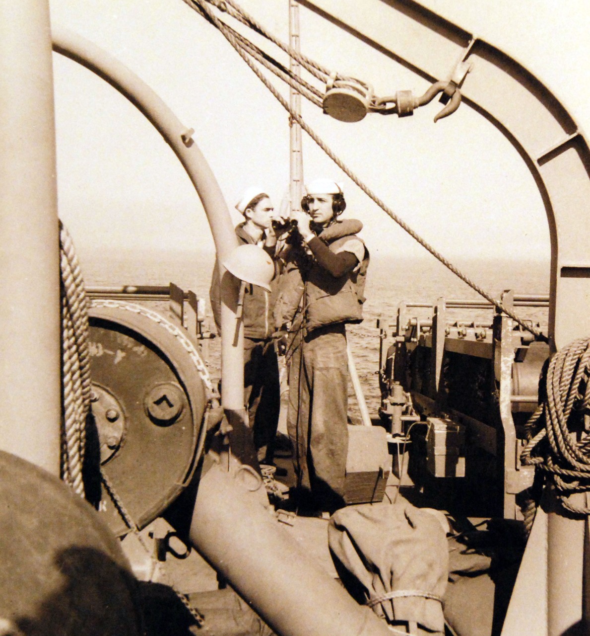 <p>80-G-14939: Battle of the Atlantic: Weapons: K-Gun Navigating USS PC-556. Depth charges onboard. Standing between the two depth charge racks on the fantail, men await orders from the bridge to adjust depth charges to explode at a given depth. One of these men will also dump the “ash cans” when given orders. In center foreground is part of a K-Gun, used to propel “ash cans” to either side of the ship, October 8, 1942.&nbsp;</p>
