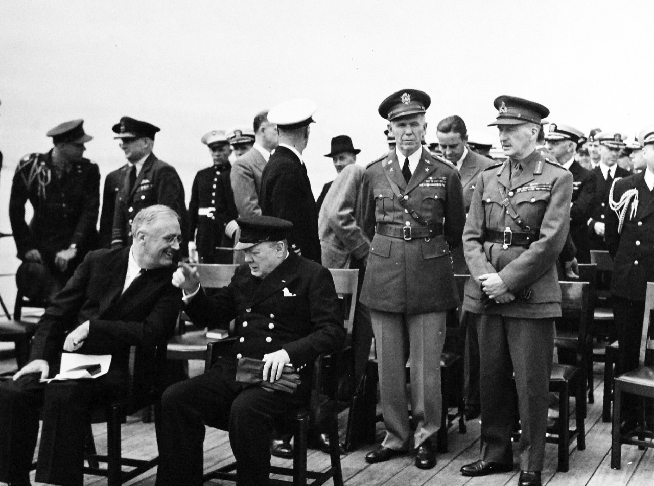 80-G-26877: Atlantic Charter, August 1941.  Informal group photograph including President Franklin D. Roosevelt and Prime Minister Winston S. Churchill on deck of HMS Prince of Wales during church services during the Atlantic Charter.  Standing, facing camera:  General George S. Marshall and General Sir John Dill. Seated: President Franklin D. Roosevelt and Prime Minister Winston S. Churchill.   Photograph released August 1941.   Official U.S. Navy Photograph, now in the collections of the National Archives.  (2016/03/22).
