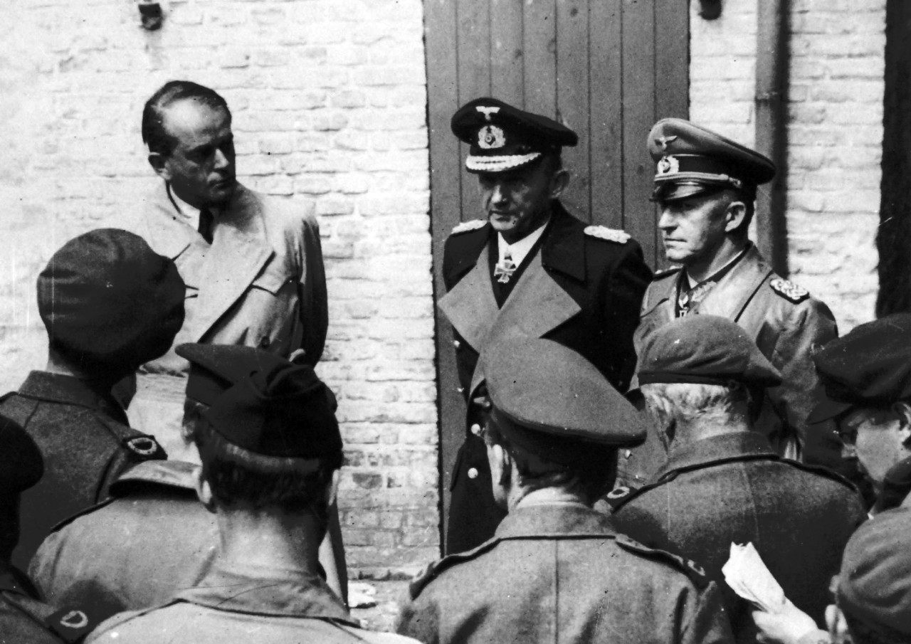 208-PU-52-P-7: Surrender of Germany,  May 1945.   Doenitz Government Arrested.   Allied war correspondents interview, left to right:  Albert Speer, Hitler’s Minister of Production; Grand Admiral Karl Doenitz, Hitler’s successor, and Colonel General Gustav Jodl, acting Commander-in-Chief of the German Army, shortly after their arrest May 24, 1945, at Flonsburg, Germany.  They were arrested by order of General of the Army Dwight D. Eisenhower, Supreme Allied Commander.  Colonel General Hans-Goorg Friedeburg, who surrendered the German Navy to the Allies, was arrested at the same time but committed suicide.  Office of War Information Photograph, now in the collections of the National Archives.  (2017/05/02). 