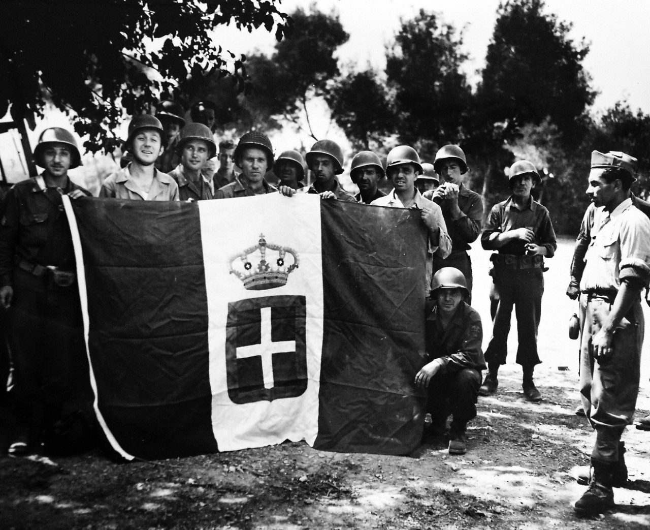 26-G-1994:   Operation Avalanche, September 1943.   Surrendered Colors.  U.S. Soldiers pose with a surrendered Italian flag for a Coast Guard photographer at a villa a few miles from the beach at Paestum, Italy.  An Italian soldier is shown at the extreme right.   Coast Guardsmen manned combat transports and landing craft in the invasion.  Official Coast Guard Photograph. Photographed through Mylar sleeve.   Courtesy of the Library of Congress: Lot-916.  (2016/05/19).