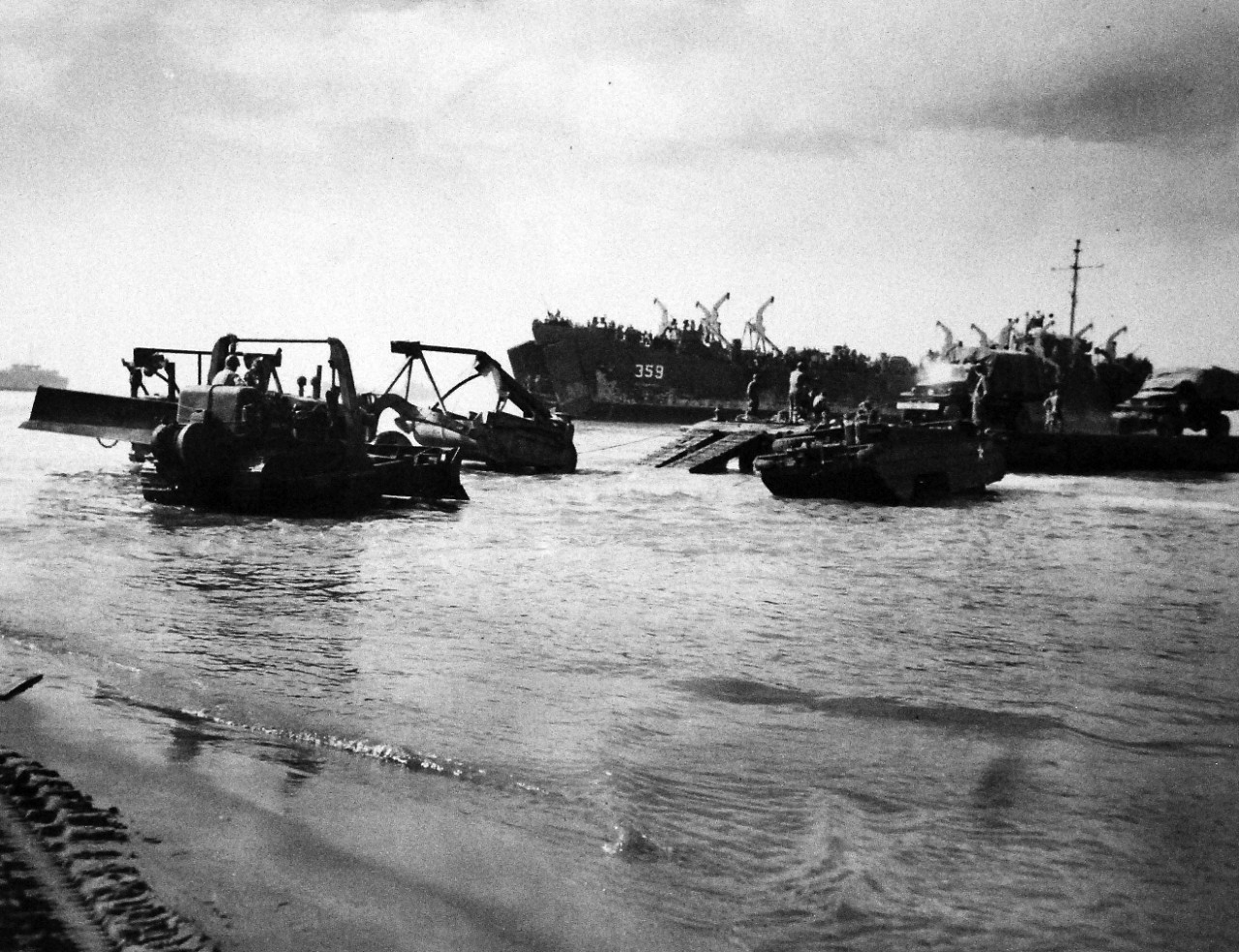 26-G-2005:   Operation Avalanche, September 1943.  Invaders Disgorged Through Bow.  Hitherto kept secret, the open doors of an LST (Landing Ship, Tanks) is shown in this photograph by a U.S. Coast Guard combat photographer.  Picture was taken at Paestum, south of Salerno, and shows bulldozers, amphibious “duck trucks” and other heavy equipment being unloaded.  The opening bow doors are probably the most revolutionary development in amphibious operations in this war.  Coast Guardsmen and Navy personnel ma LSTs and other landing craft.     Official Coast Guard Photograph, RG-G-2005. Photographed through Mylar sleeve.   Courtesy of the Library of Congress.  (2016/05/19). 
