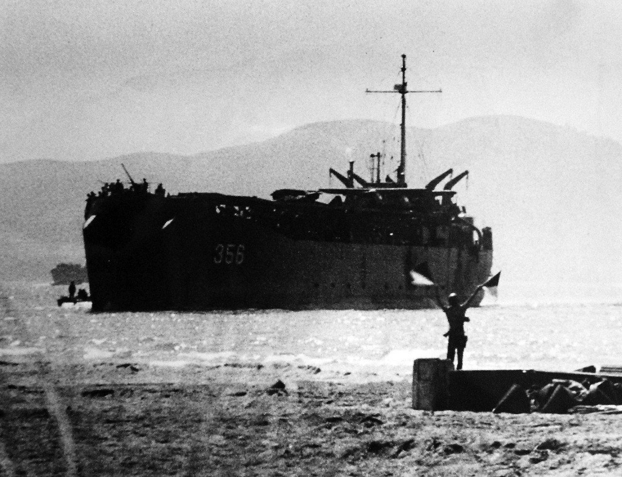 26-G-92443-1:   Operation Avalanche, September 1943.  “Talking” Off Paestum.  A U.S. Coast Guardsman signals to USS LST 356 whose bow doors yawn empty off Paestum, twenty miles south of Salerno, as the invasion gets under way.  This picture shows the open bow doors – hitherto a closely guarded military secret.   The ship has already discharged its cargo of motorized equipment .  Coast Guard and Navy personnel the LST craft.   Official U.S. Coast Guard Photograph. Photographed through Mylar sleeve.   Courtesy of the Library of Congress.  (2016/05/19). 