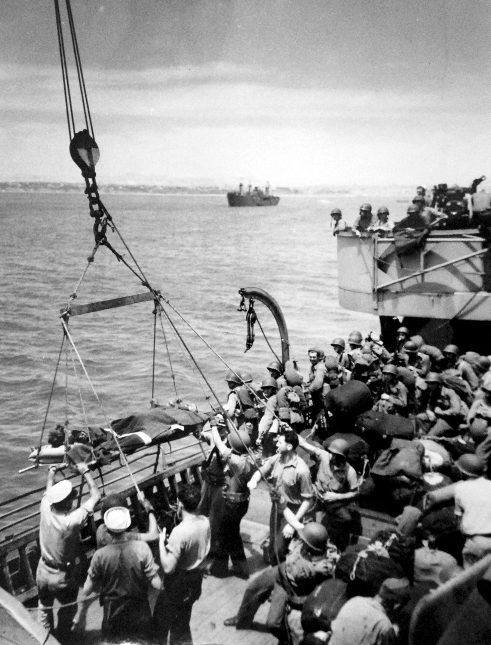 26-G-1796:  Operation Husky - Invasion of Sicily, July – August 1943.    While wounded are brought back to a U.S. Coast Guard manned transport, other soldiers aboard the ship are ready to take their turn to join the invaders of Sicily.   U.S. Coast Guard Photograph.  Photographed through Mylar sleeve.  Courtesy of the Library of Congress:   Lot-805-9. (2015/10/30).