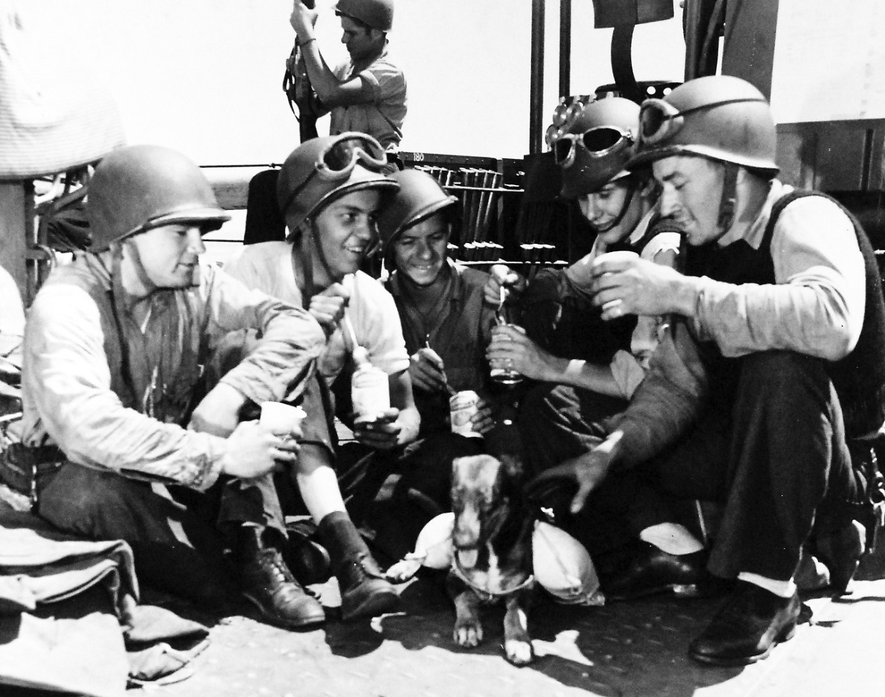 80-G-42519:  Operation Husky, July-August 1943. Helmeted American soldiers relax from before-battle tension by breaking out canned rations.  Troops mascot, wearing a canine lifejacket, doesn’t seem attracted by the prospect of such food.    Photographed:  July 1943.  Official U.S. Navy photograph, now in the collections of the National Archives.  (2016/05/17). 