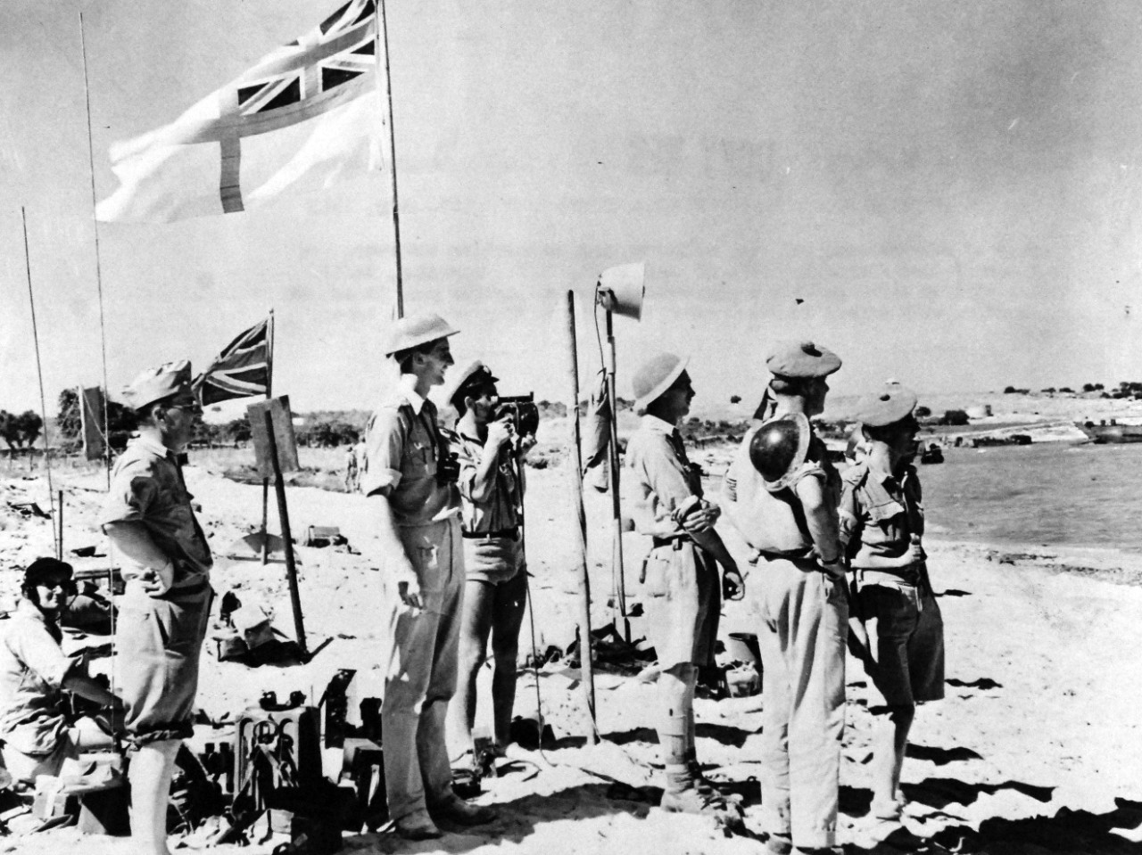 80-G-42797:  Operation Husky, July-August 1943.  British Army and Navy Officers and an American observer, Commander Walter Chappell, USNR, (standing left) liaison officer with the Eighth Army – watch landing parties pour in as they stand at a beach signal station, where the British flag has just been planted during the Sicilian Invasion, July 1943.   Official U.S. Navy Photograph, now in the collections of the National Archives.   (2017/08/01).  