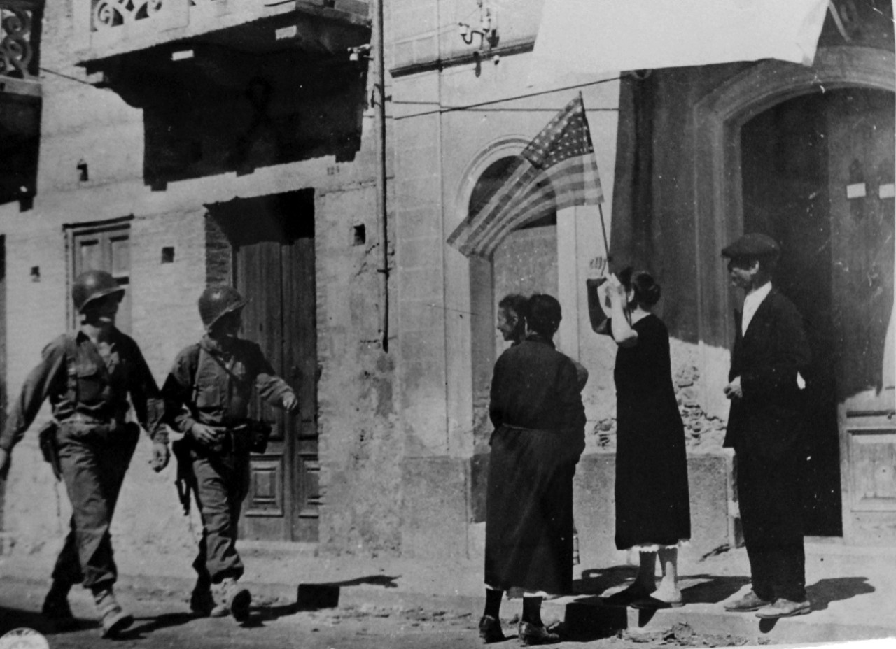 LC-USZ62-97663: Operation Husky - Invasion of Sicily, July-August 1943. Two U.S. Army soldiers walk towards four native civilians, including a woman holding a U.S. Flag.  U.S. Army Photograph. Courtesy of the Library of Congress: Lot-805.   (2015/10/30).