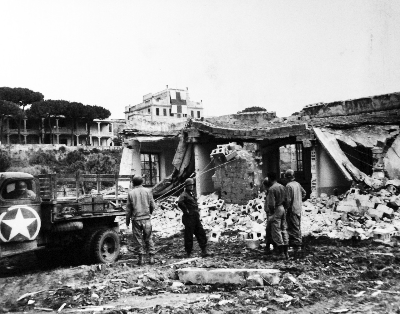 80-G-59383:   Battle of Anzio, January-June 1944 .    A giant Red Cross insignia over a front-line hospital dominates this scene at an Anzio beachhead.  In the foreground, US Army men inspect the ruins of a recently shelled building to look for the injured or dead, February 1944.  Photograph received 25 April 1944.  Official U.S. Navy Photograph, now in he collections of the National Archives.  (2014/03/12).    
