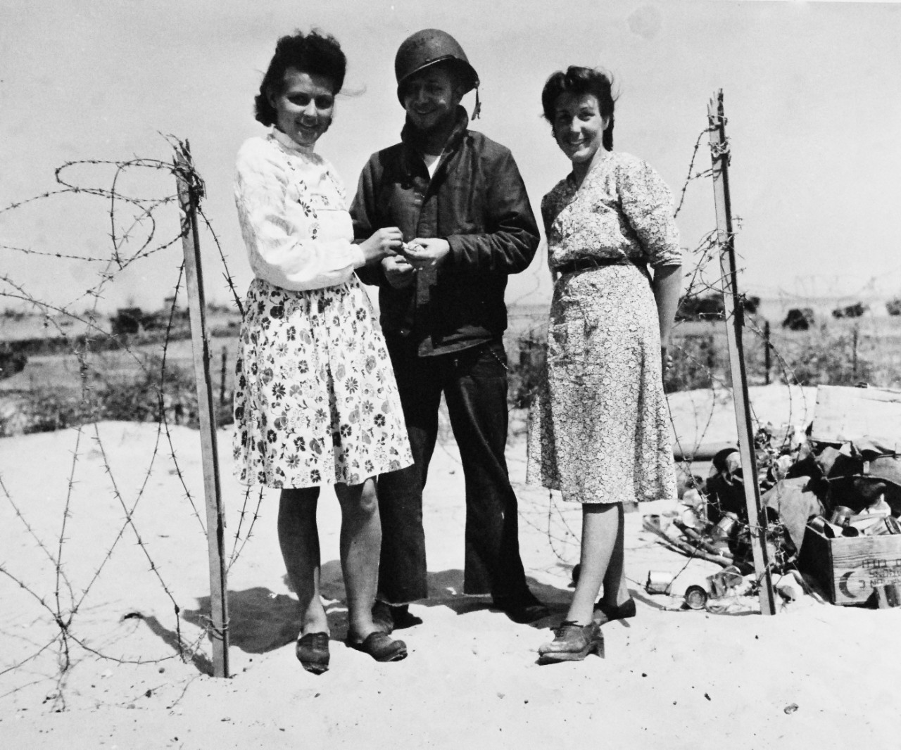 80-G-255949:   Normandy Invasion, Cherbourg, France, July 1944.    French girls accept cigarettes from an American sailor on beach-head in France.  These girls were found aiding in operations of radio receiving and transmitting. Photographed by CPU-11, 15 June 1944.  Official U.S. Navy Photograph, now in the collections of the National Archives.   (2014/11/05). 