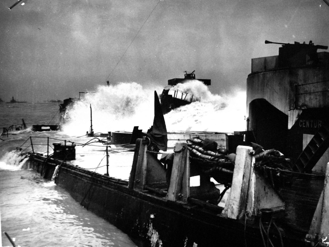 26-G-2963: Normandy Invasion, Mulberries, June 1944.  Violent Storm Battered Normandy Breakwater of Sunken Freighters during Invasion Landings.  Reducing the violence of a storm that blew in upon Normandy invasion operations soon after D-Day, a breakwater of sunken freighters shielded Allied landings and cut down the toll of destruction.  Coast Guard officers, thoroughly briefed in their job, helped direct the planned sinking of 23 ships to form a breakwater.   Photographed from a Coast Guard LCI (L) shows a mountainous wave spending its fury against the bulwark, June 1944.  Official U.S. Coast Guard Photograph, now in the collections of the National Archives.   (2015/5/19).  