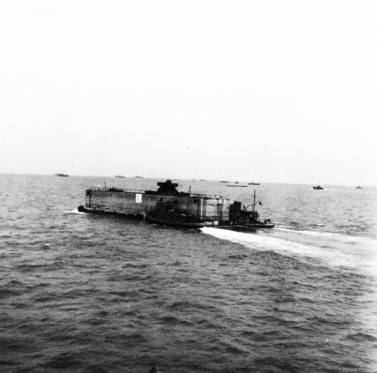 80-G-285191:  Normandy Invasion, Mulberries, June 1944.   The Phoenix or sectional concrete breakwater forming part of the U.S. Mulberry for man-made harbor off Omaha Beach, France, protecting landing craft from storms of English Channel.  Shown: The Phoenix being towed in to be sunk at the beach.  Photograph released November 7, 1944.  Official U.S. Navy photograph, now in the collections of the National Archives.  (2016/03/15).