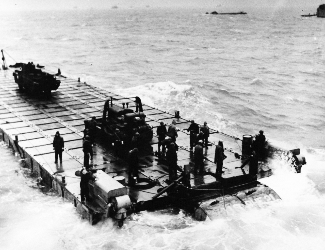80-G-45670:  Normany Invasion, Rhino Ferry, June 1944.   “Rhino Ferries,” designed by Navy’s Civil Engineering Corps to bridge the gap between ship and shore, are pontoons owered by two outboard motors of 143 hp and complete with steering gear.  Ferries are formed of 30 pontoons in length by 6’ wide, displaced approximately 275 tons, speed of about 4 knots and a shallower draft than LST’s.   Consisting of a series of five by seven by five cubes of welded steel, pontoons can withstand loads equal to civil highway bridges.   Photograph released June 6, 1944.    Official U.S. Navy Photograph, now in the collections of the National Archives.  (2014/9/9).  