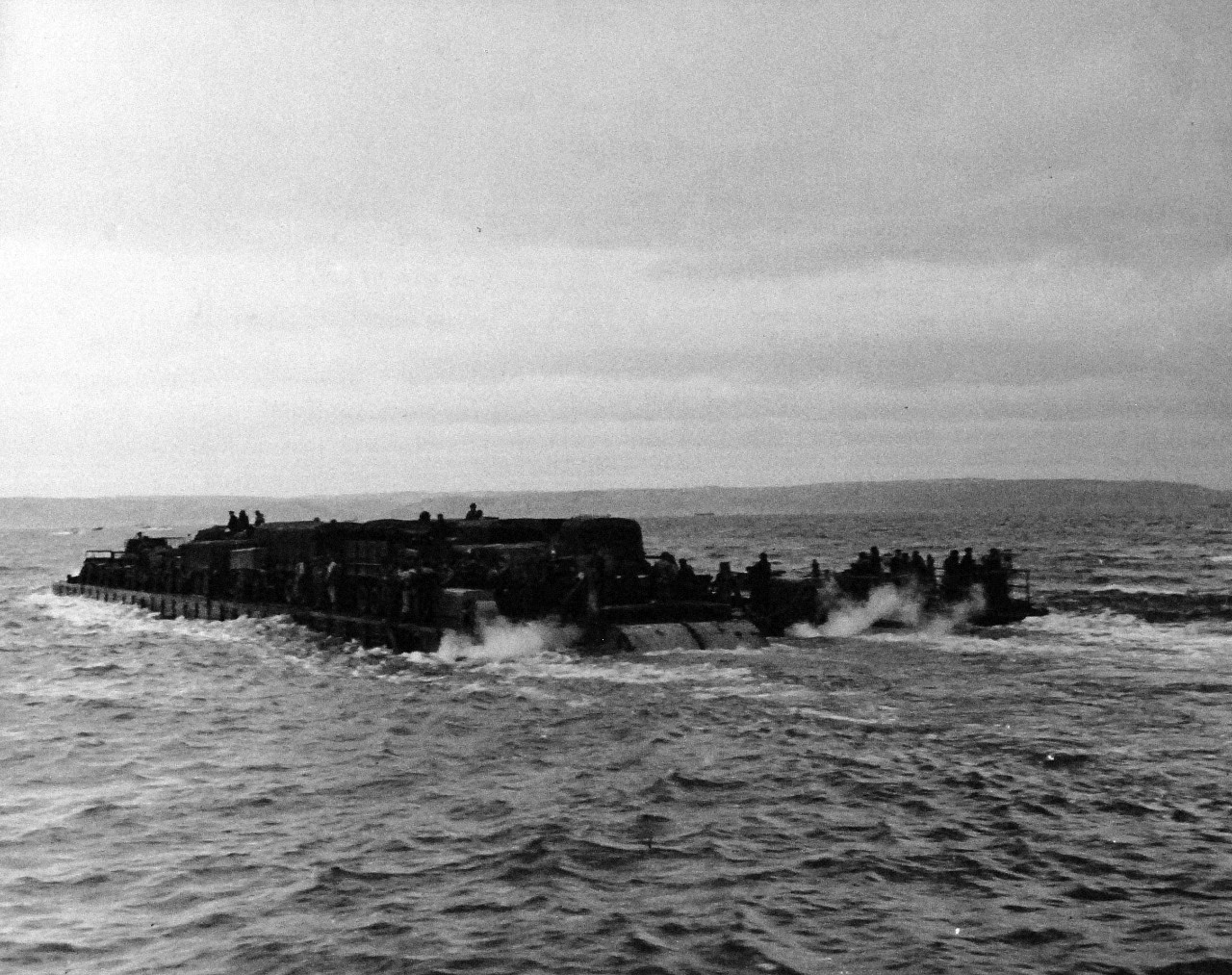 80-G-59399:  Normany Invasion, Rhino Ferry, June 1944.     “Rhino Ferries” designed by Navy’s Civil Engineer Corps to bridge the gap between ship and shore, are pontoons powered by two outboard motors (143hp) and complete with steering gear.   Ferries are formed of 30 pontoons in length and by 6 wide.  The displacement is approximately 275 feet long and has 4 knots, but with a shallower draft than LSTs, photograph dated June 6, 1944. Official U.S. Navy Photograph, now in the collections of the National Archives.    (2014/3/12).   