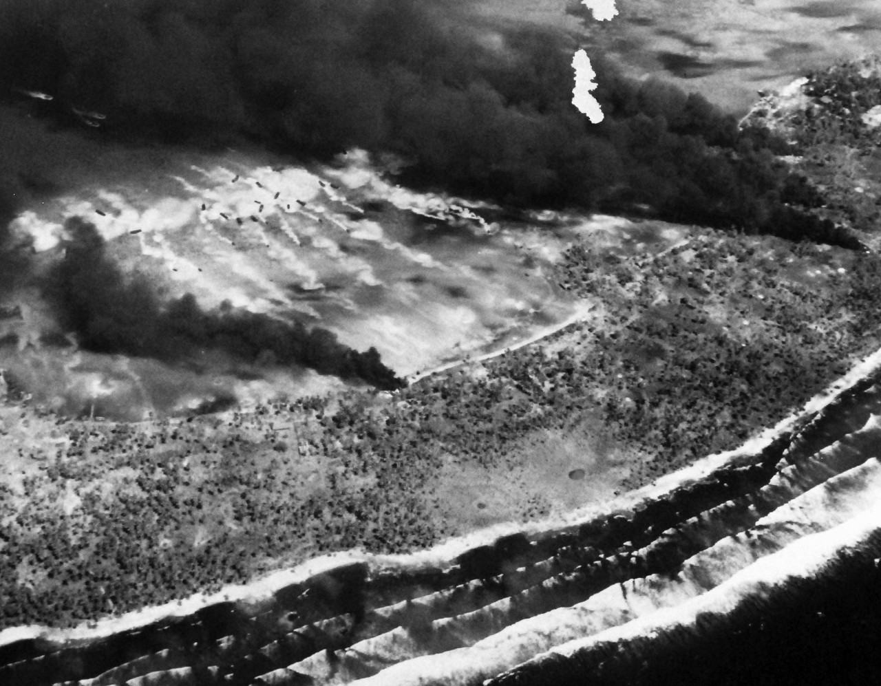 80-G-204716:  Operation Galvanic, November 1943.      Oblique of damage done to enemy positions on Makin Island, Gilbert Islands by bombing and bombardment, 20-21 November 1943 by U.S. forces.   Shell or bomb craters, old hulks, house, revetments.  Smoke from four bomb hits partially hiding the boats.  350 degrees.   Official U.S. Navy Photograph, now in the collections of the National Archives.  (2013/09/19).