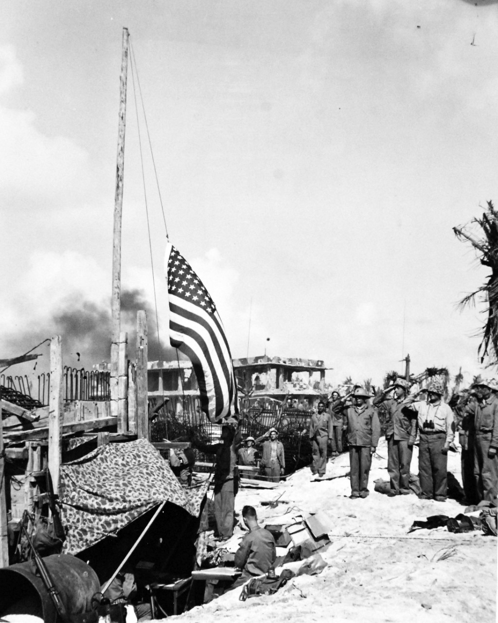 80-G-208974:  Operation Flintlock, January-February 1944.    Fourth Marine Division attack on Roi Island, Kwajalein Atoll, Marshall Islands, February 1-2, 1944.   Shown:  U.S. Marines halt to salute the flag as it goes up soon after the capture of the Marshall islands stronghold from the Japanese.  In the background is the remains of a three-story concrete block-house knocked out by the terrific bombardment by land, sea, and air.    Official U.S. Navy photograph, now in the collections of the National Archives.  (2017/07/25).  