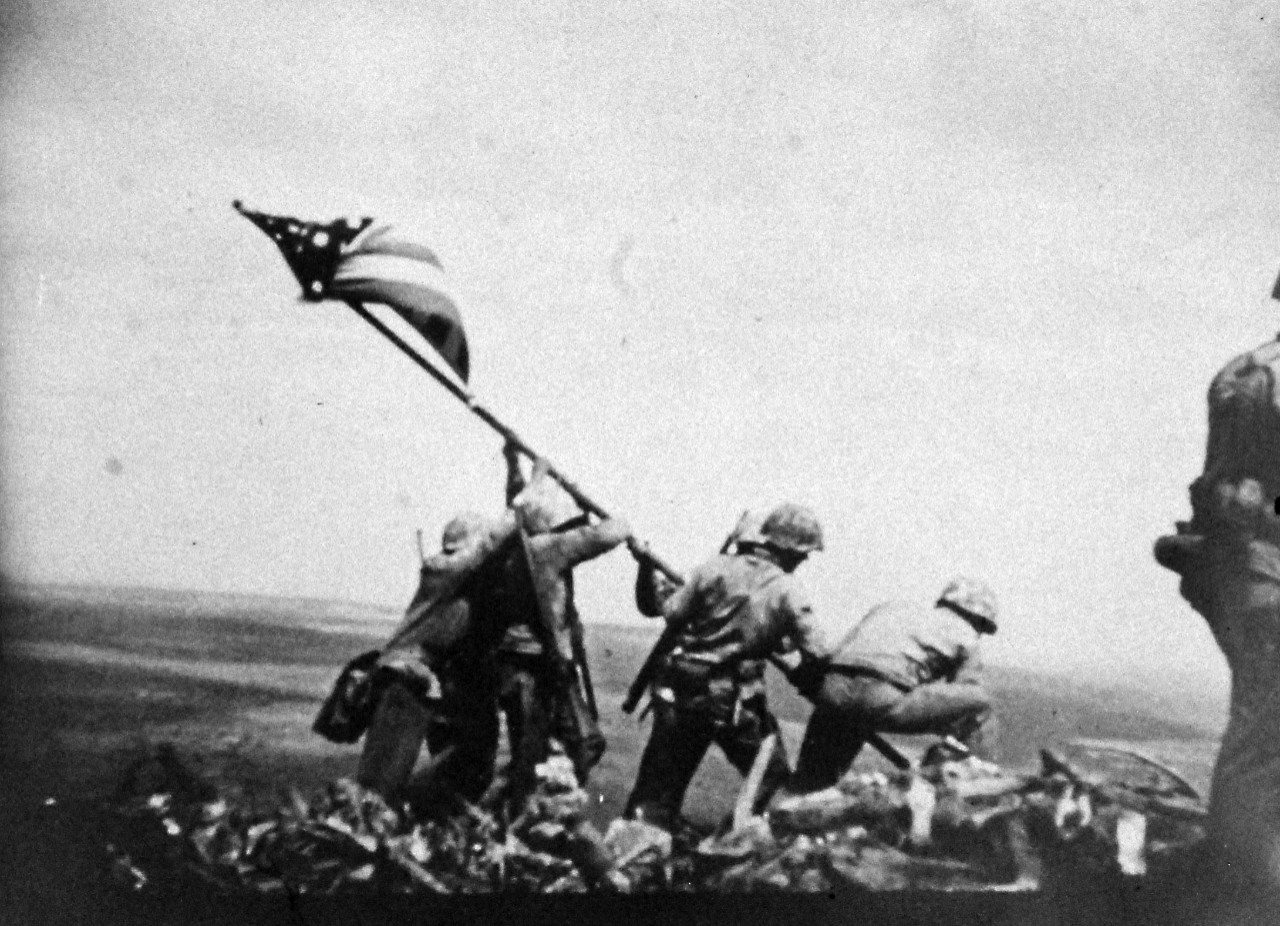 127-GW-319-116772:   Iwo Jima Operations,  February 1945.  Over Suribachi.  A “still” taken from the 16mm movie series of the U.S. Marines raising the American flag on the summit of Mount Suribachi, Iwo Jima.     Photographed by Genaust, February 23, 1945.   Official U.S. Marine Corps Photograph, now in the collections of the National Archives.  (2016/09/06).