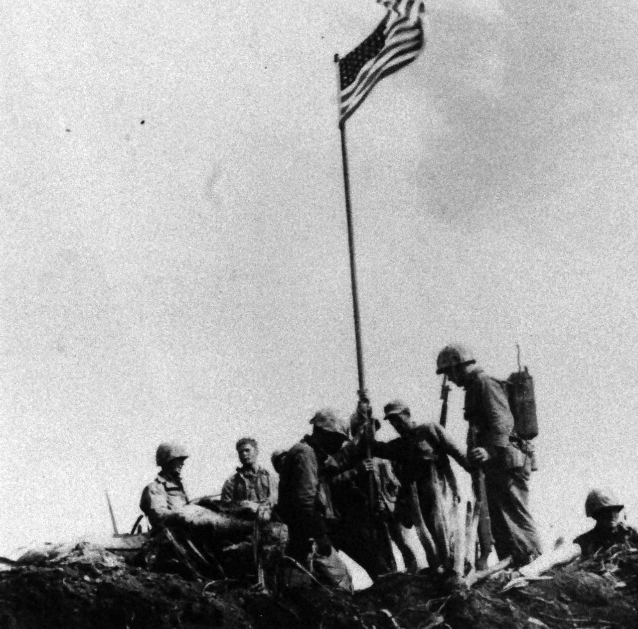 127-GW-319-A708068:   Iwo Jima Operations, February 1945.  U.S. Marines of First Lieutenant Harold G. Schrier’s patrol, Co. “E”, 2nd bn, 28th Marines, moments after raising the First Flag atop Mt. Suribachi.  Identifiable U.S. Marines are: Private First Class Gene M. Marshall, carrying radio and Sergeant Henry O. Hansen, immediately to the left of Private First Class, Marshall, wearing utility cover, with right hand on flag pole.   Photographed by Sergeant L.R. Lowery, February 23, 1945.   U.S. Marine Corps Photograph, now in the collections of the National Archives.   (2016/09/06).