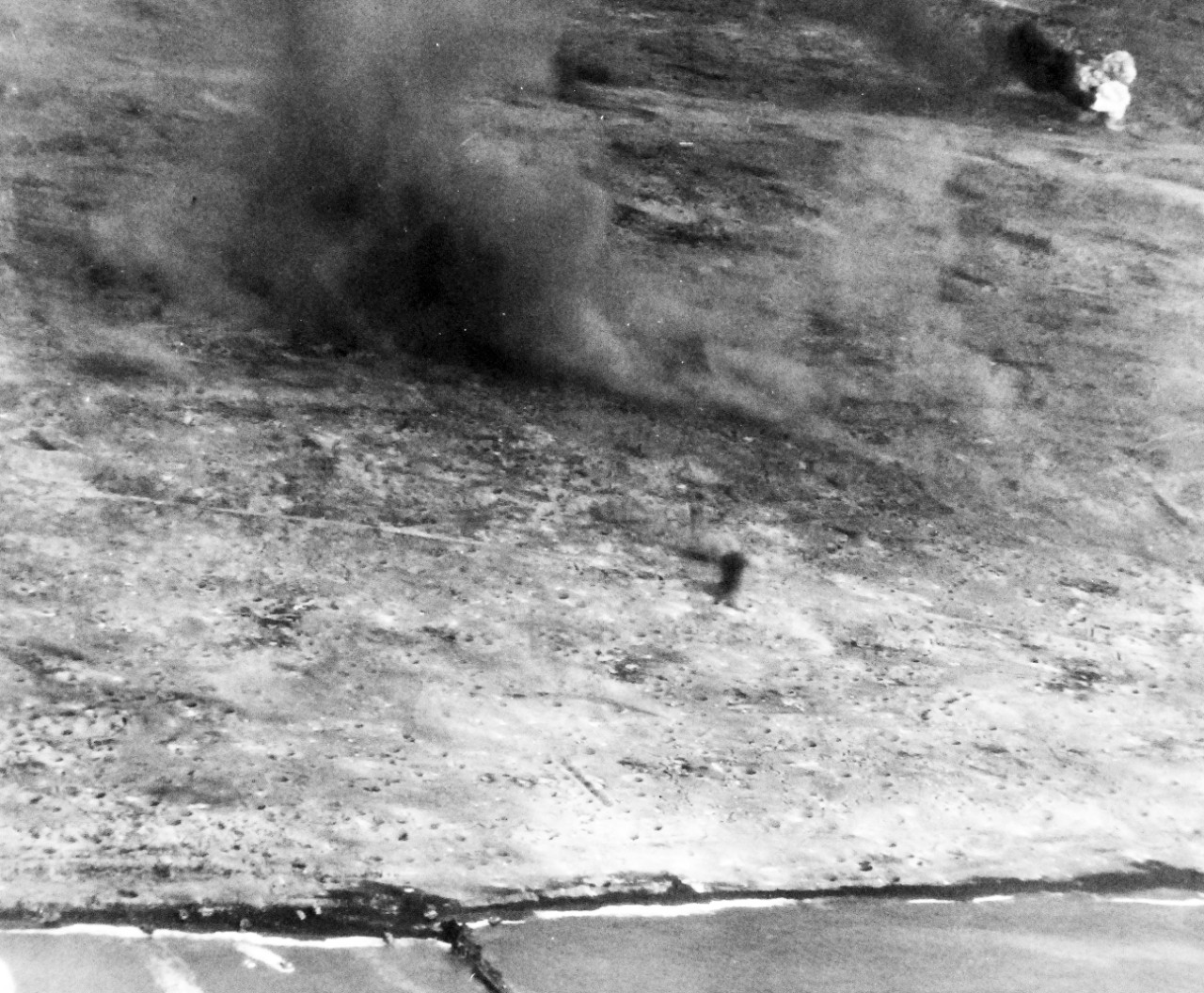 80-G-307196: Battle for Iwo Jima, February 27, 1945. Iwo Jima covered with bomb craters from incessant attack by carrier based planes.  Note smoke rising and aerial field in background.  Photographed by plane from USS Saginaw Bay (CVE-82).   U.S. Navy photograph, now in the collections of the National Archives.  (2016/09/06).