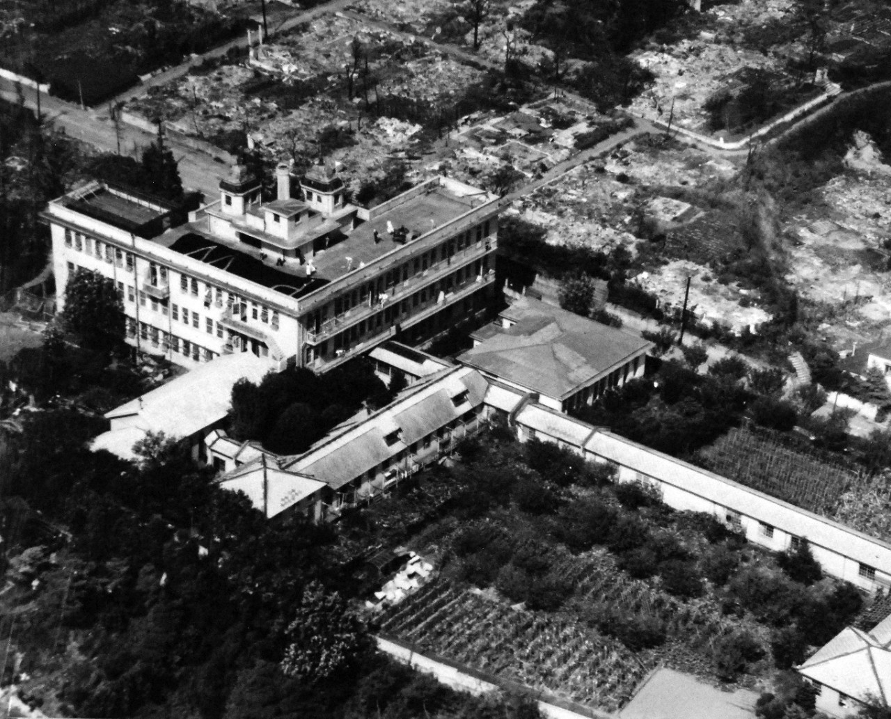 80-G-344489:   Allied Prisoner of War Building, Tokyo, Japan, 1945.    Prisoner of War building at Tokyo, Japan, with people on the roof.  Taken by plane from USS Essex (CV-9), PHOM1/C P.J.Madden, PHOM3/C H.C. Stoker, August 28, 1945. Official U.S. Navy photograph, now in the collection of the National Archives.  (2014/05/22).    The original photograph is small.   