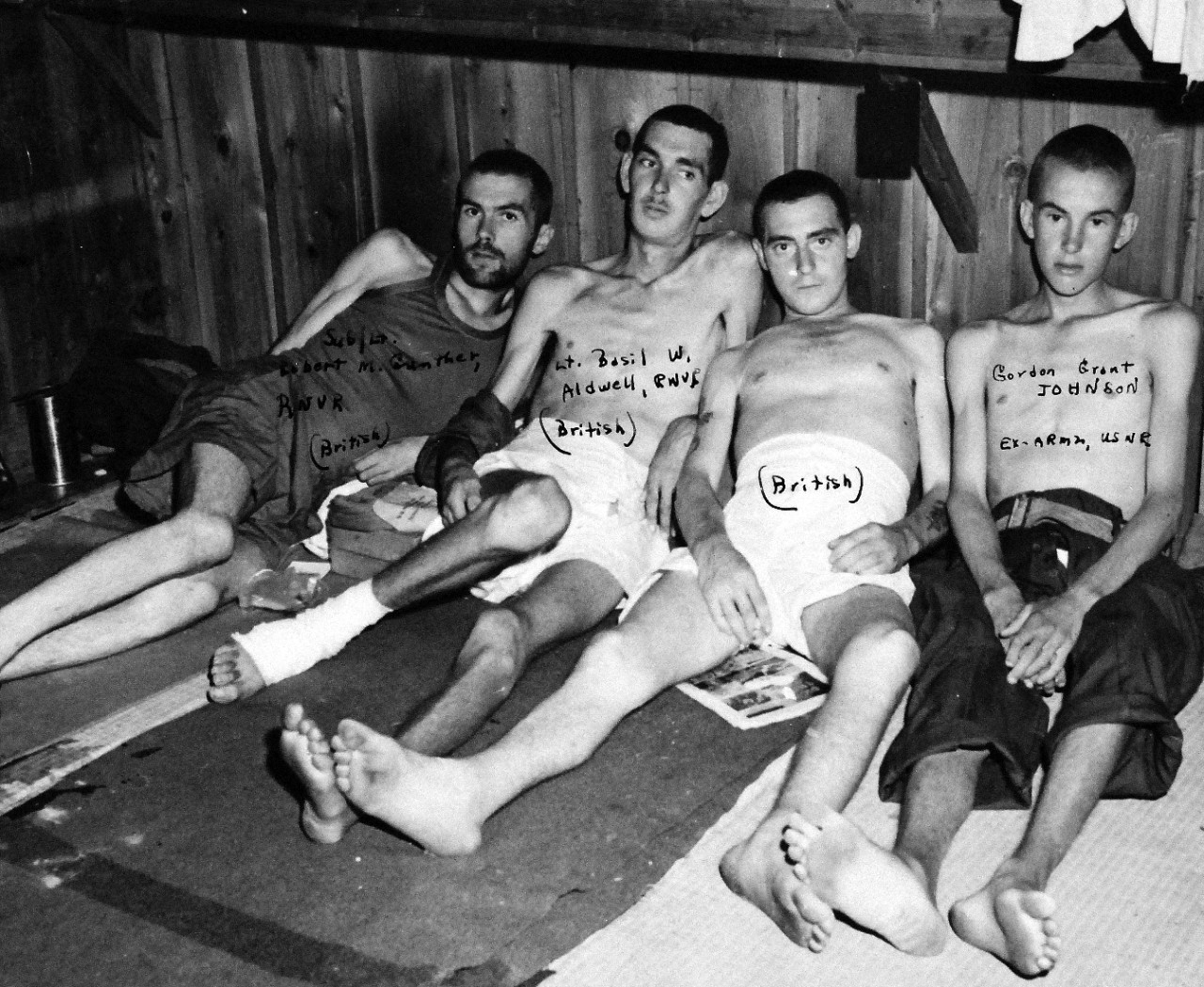 80-G-490448:  Allied Prisoner of War Camp, Omori, Japan, 1945.  Allied prisoners of war, suffering from malnutrition and other disorders as seen after their rescue from the Omori Camp, Tokyo, Japan, area by a U.S. Navy Rescue Mission headed by Robert Simpson and Commander Harold Stassen.  Treatment of the prisoners was described as inquisitional form of barbarism.  Four gaunt Allied prisoners weakly hold themselves up in their beds.  Left to right:  Sub/Lieutenant; Robert M. Gunther, RNVR (British); Lieutenant Basil W. Aldwell, RNVR (British); Unknown (British); and Ex-ARM2 Gordon Grant Johnson, USNR.  Released August 29, 1945.  Official U.S. Navy photograph, now in the collection of the National Archives.   (2015/11/10).
