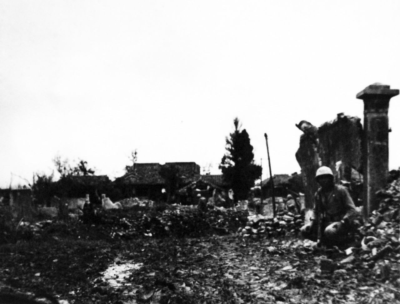 127-GW-518-122300:   Okinawa Campaign, April-June 1945.     Fourth Marines, “L” Company Rifle Squad, lie low and break up while making way near river bank at Naha, Okinawa, 24-26 May 1945.  At time photograph was taken Japanese were putting everything they had at the Marines.  Note, large explosions in Naha made by our planes and heavy artillery.   Official U.S. Navy Photograph, now in the collections of the National Archives.   (2014/6/25).