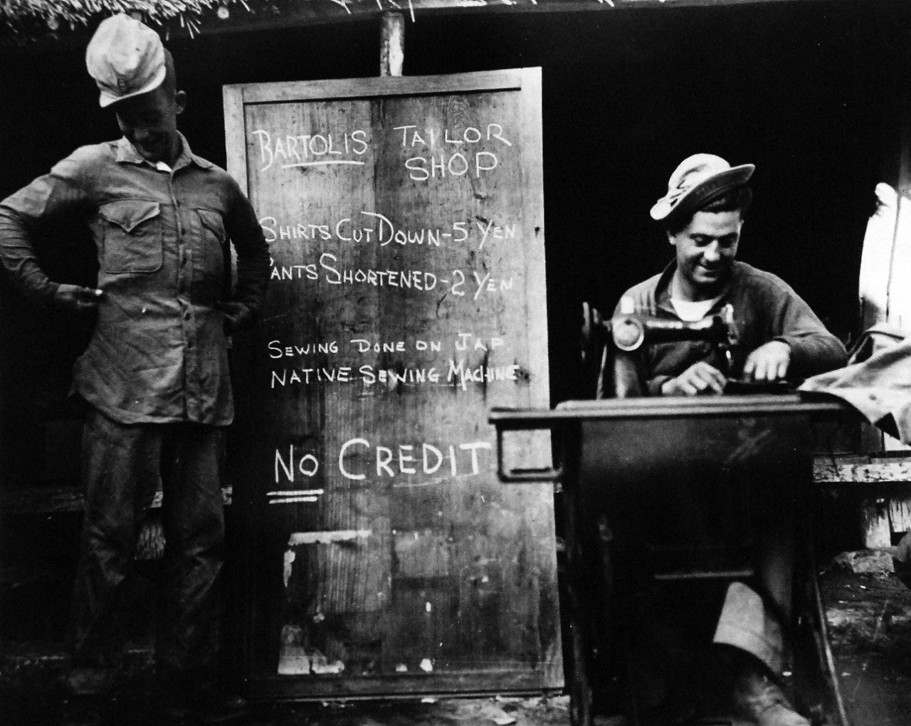 80-G-322707: Marine Sergeant Renato “Bart” Bertoli, (right), uses a Japanese sewing machine on Okinawa, Ryukyu Islands.  Private L.E. Buck, (left), one of Bartoli’s satisfied customers, tries on a shirt.  Both men are attached to the First Marine Division, released April 22, 1945.  U.S. Navy photograph, now in the collections of the National Archives.  (2016/04/26).  