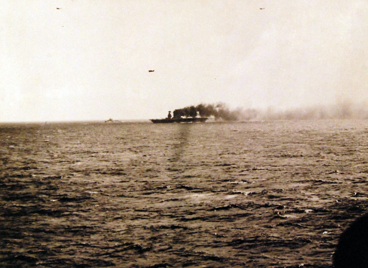 80-G-16643:   Battle of the Coral Sea, May 1942.   USS Lexington (CV-2) afire and down at the bow, but still steaming and operating aircraft, shortly after she was hit by Japanese torpedoes and bombs during the Battle of the Coral Sea.  This view was taken about Noon on 8 May 1942, before fires were extinguished from a bomb hit on the carrier's smokestack.  Plane overhead is a Grumman F4F "Wildcat" fighter.  Official U.S. Navy Photograph, now in the collections of the National Archives.   (4/10/2014).